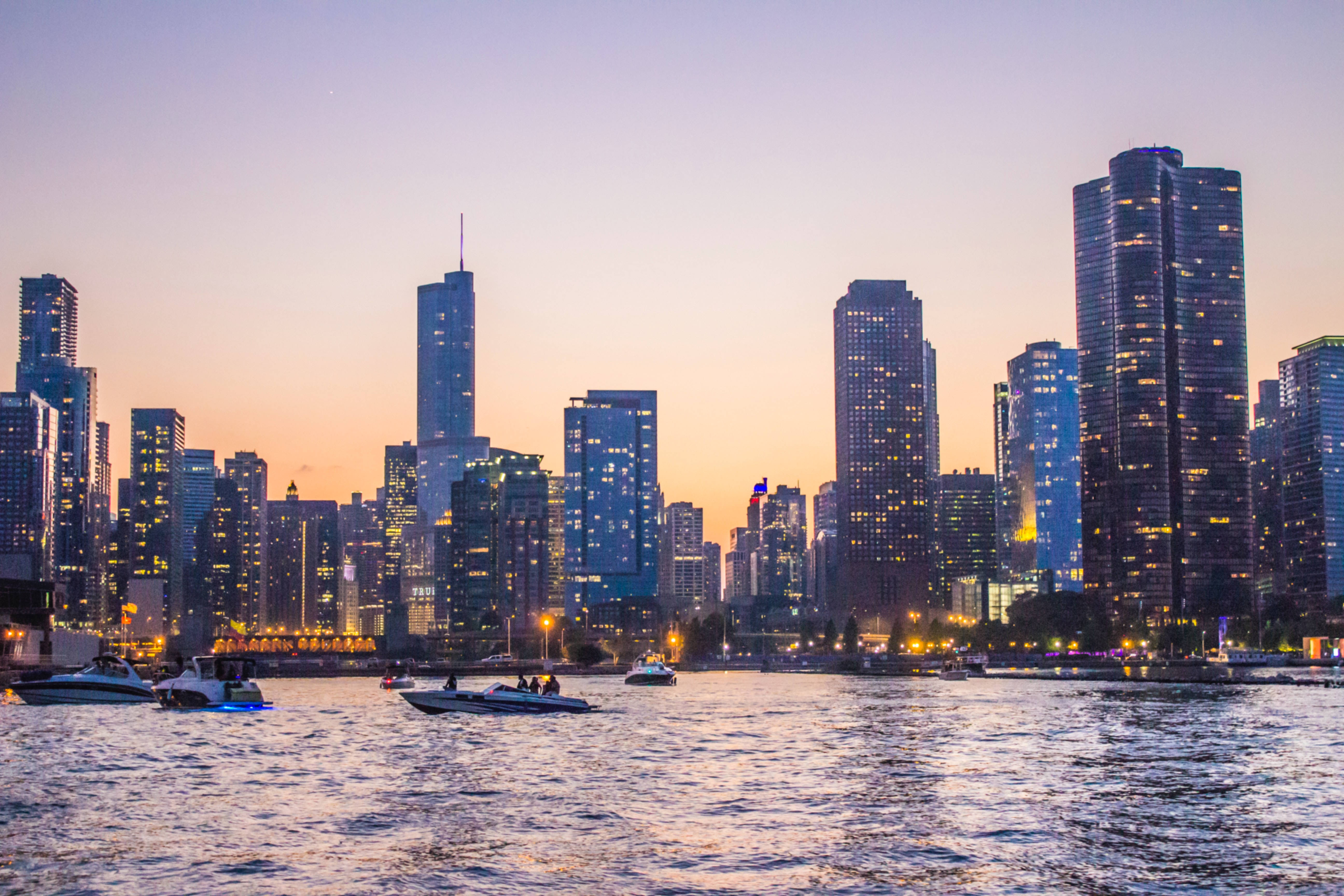 Chicago Skyline 桌布 壁紙 — 黃昏時分的城市天際線，發光的摩天大樓倒映在水中，船隻在港口滑行。
