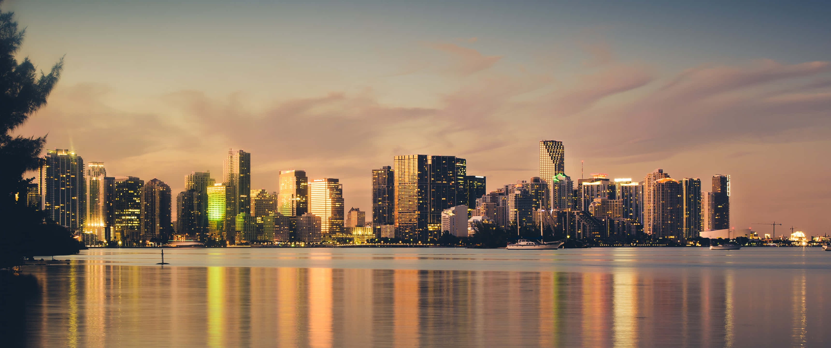 Miami 4K 桌布 壁紙 — 黃昏時分的城市天際線全景，燈火通明的摩天大樓倒映在平靜的水面上。