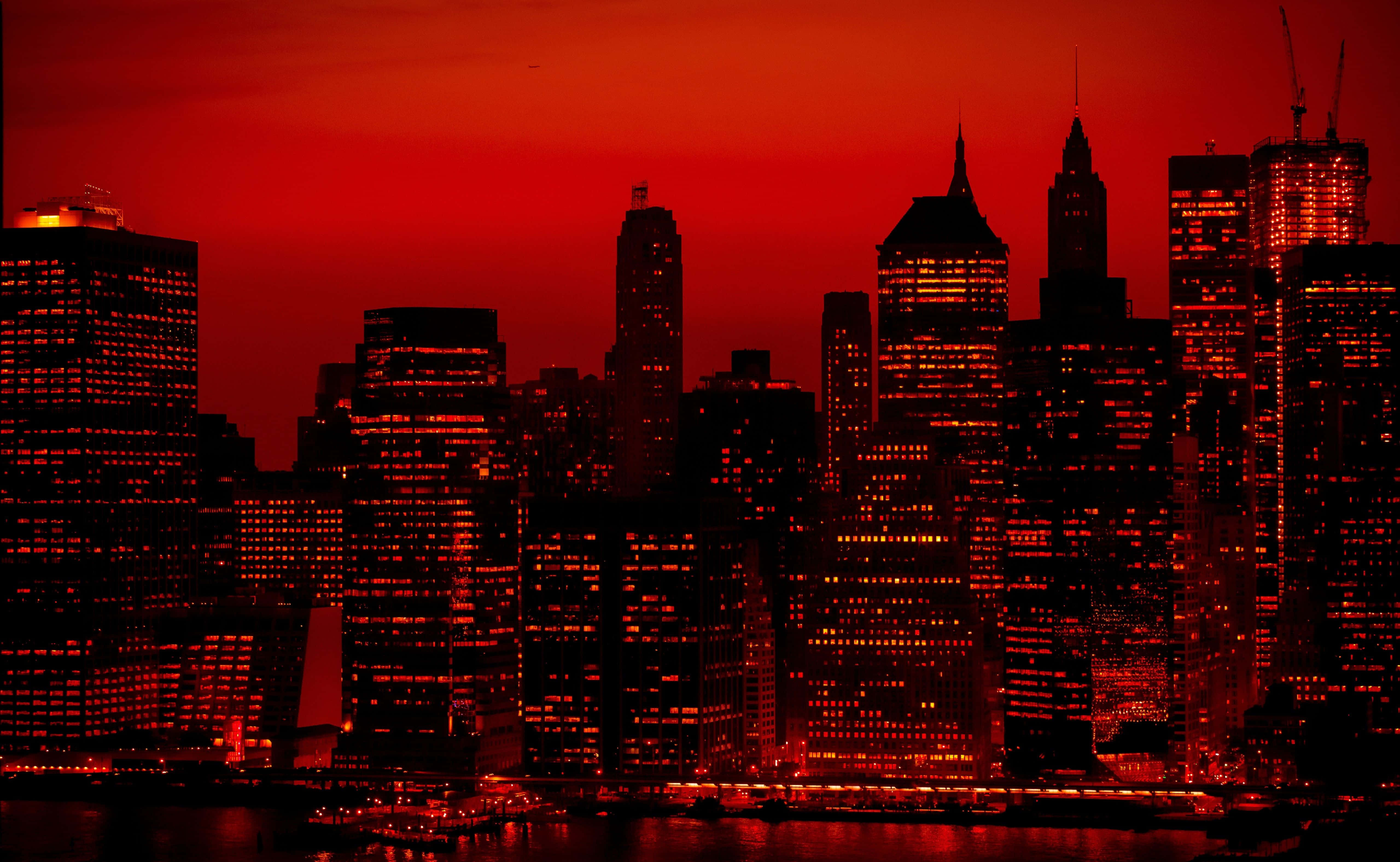 New York Skyline 桌布 壁紙 — 黃昏時分的城市天際線沐浴在火紅的光芒中，明亮的窗戶倒映在下方水面上。