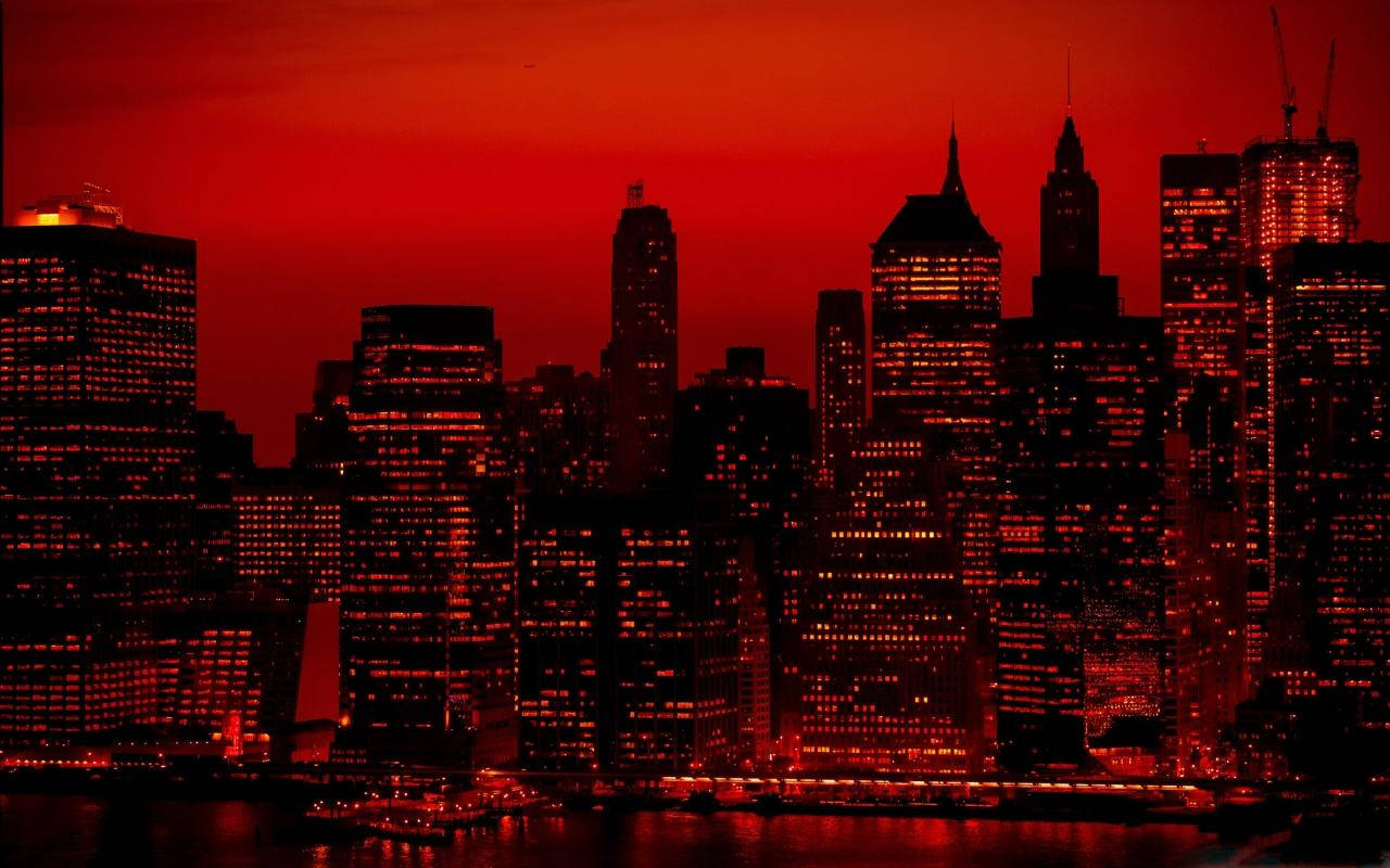New York 桌布 壁紙 — 黃昏時分的城市天際線沐浴在火紅色的光芒中，明亮的窗戶倒映在下方水面上。