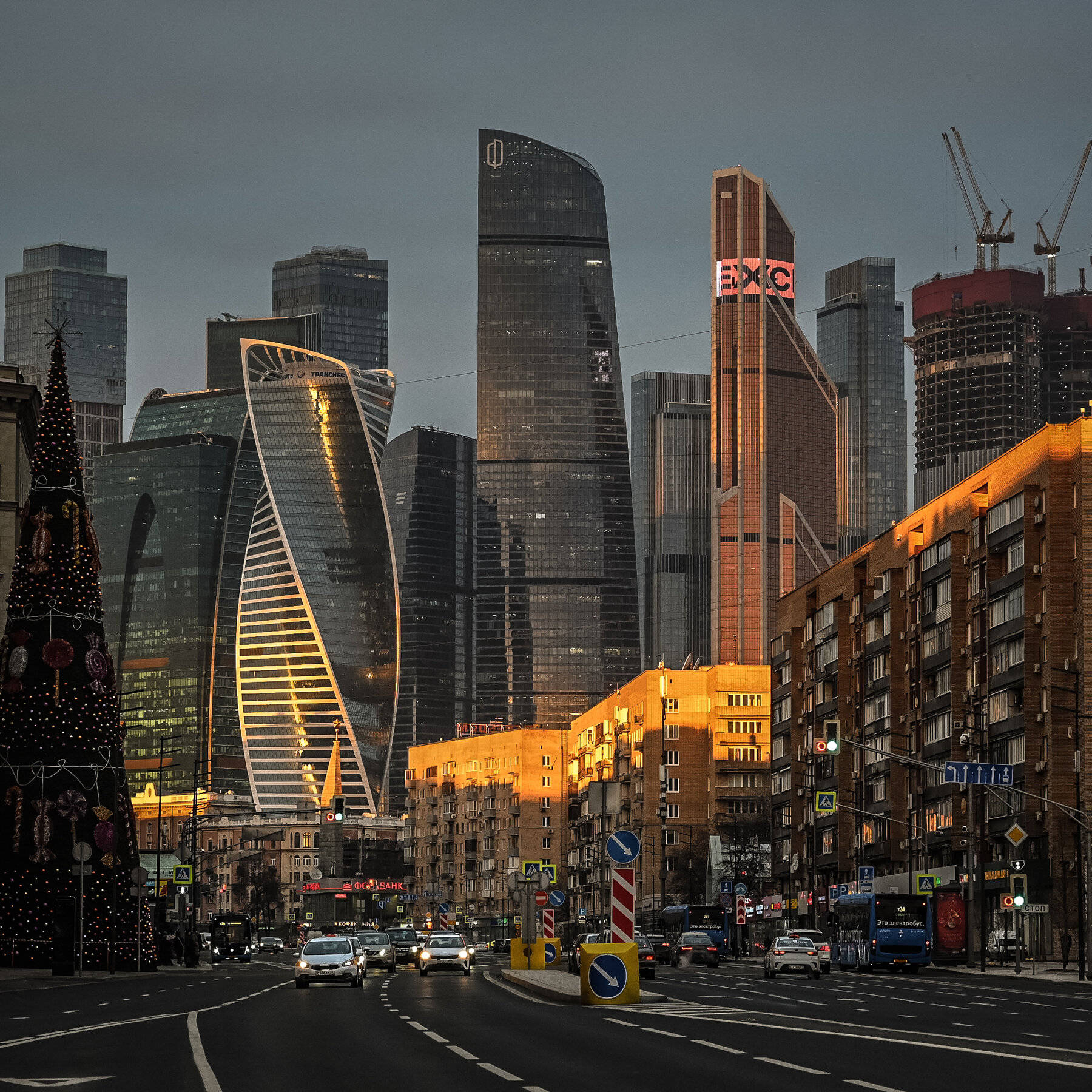 Moscow 桌布 壁紙 — 黃昏時分的城市街道，現代玻璃摩天大樓反射著金色光芒，人行道上有一棵裝飾好的聖誕樹。
