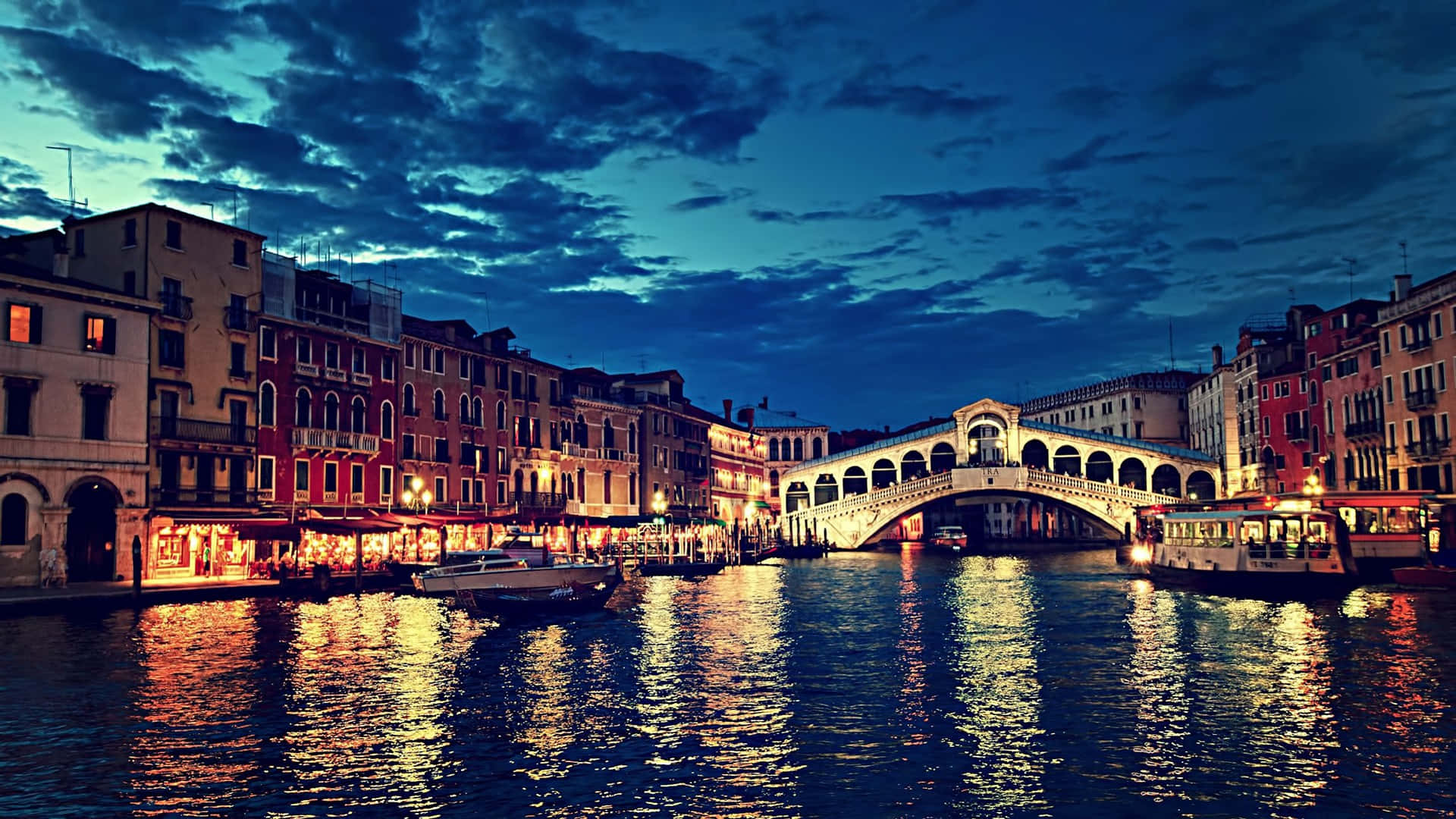 Italy Aesthetic 桌布 壁紙 — 黃昏時分的威尼斯，里亞爾托橋在溫暖燈光下閃耀，倒映在運河水中。