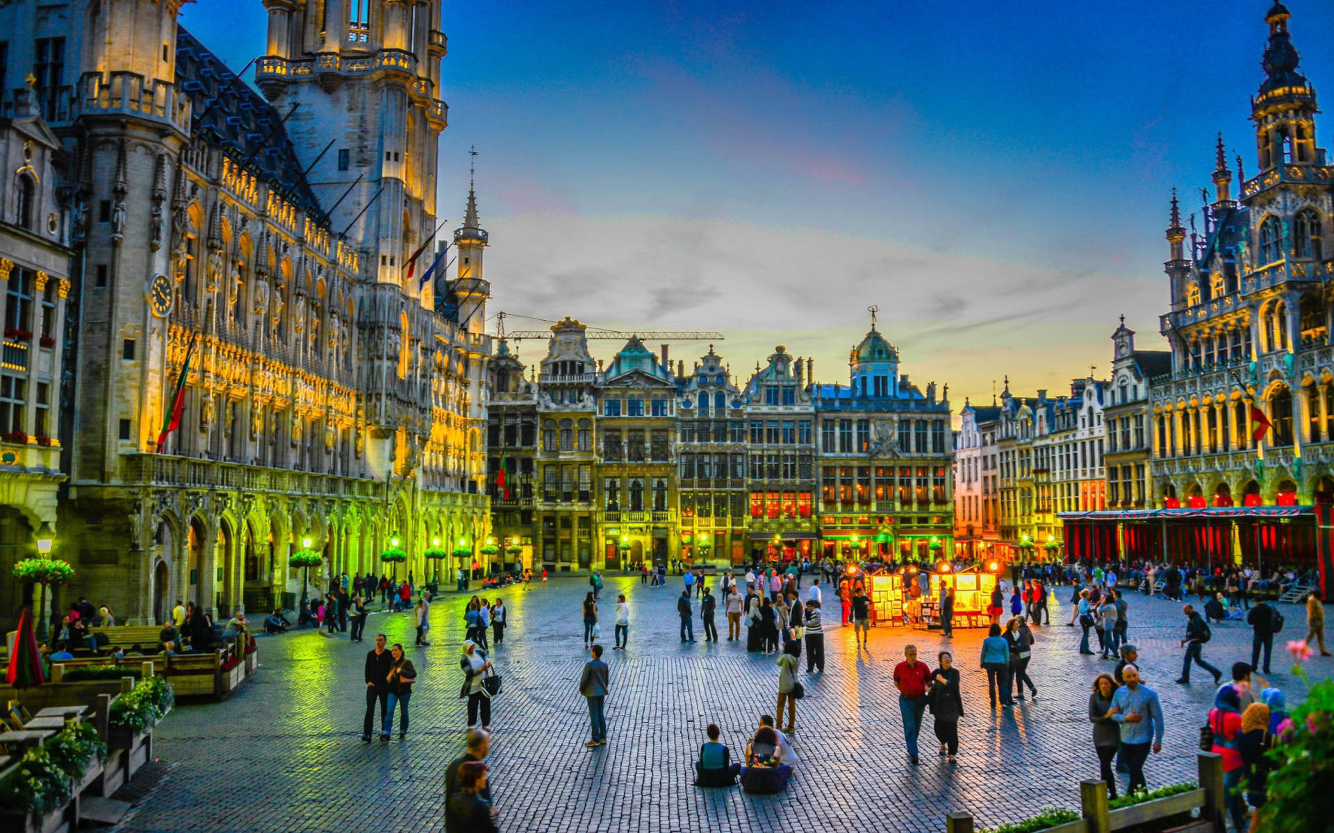 Belgium 桌布 壁紙 — 黃昏時分的宏偉歷史廣場，華麗建築溫暖地發光，人們在鵝卵石廣場上漫步。