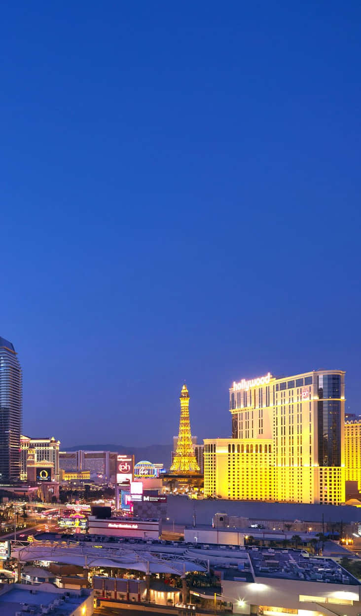 Las Vegas Phone 桌布 壁紙 — 黃昏時分的拉斯維加斯天際線，金色艾菲爾鐵塔複製品和發光的酒店映襯著深藍色的天空。