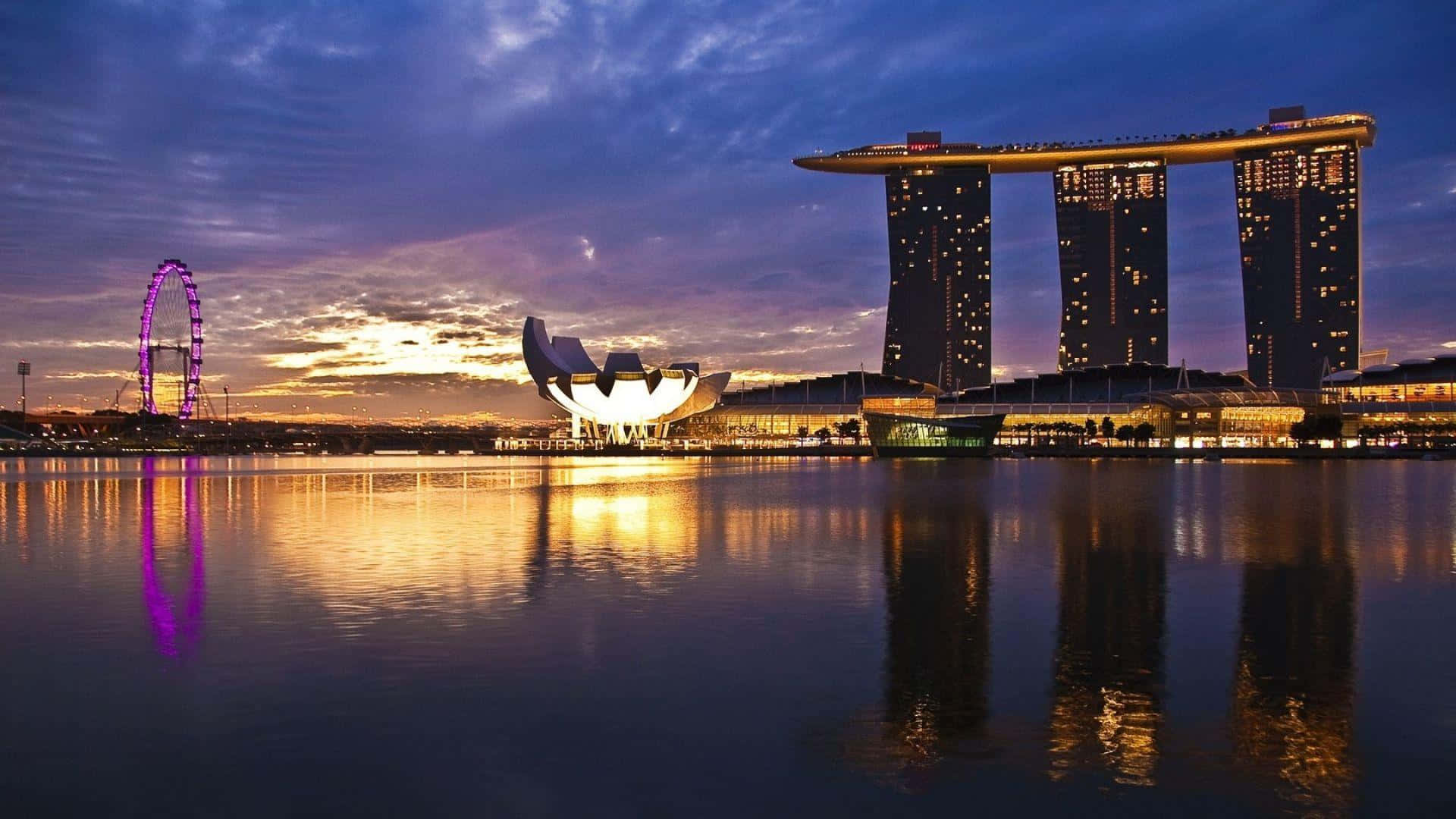 Singapore 桌布 壁紙 — 黃昏時分的新加坡天際線，濱海灣金沙和藝術科學博物館在紫色和金色天空下平靜的水面上倒映。
