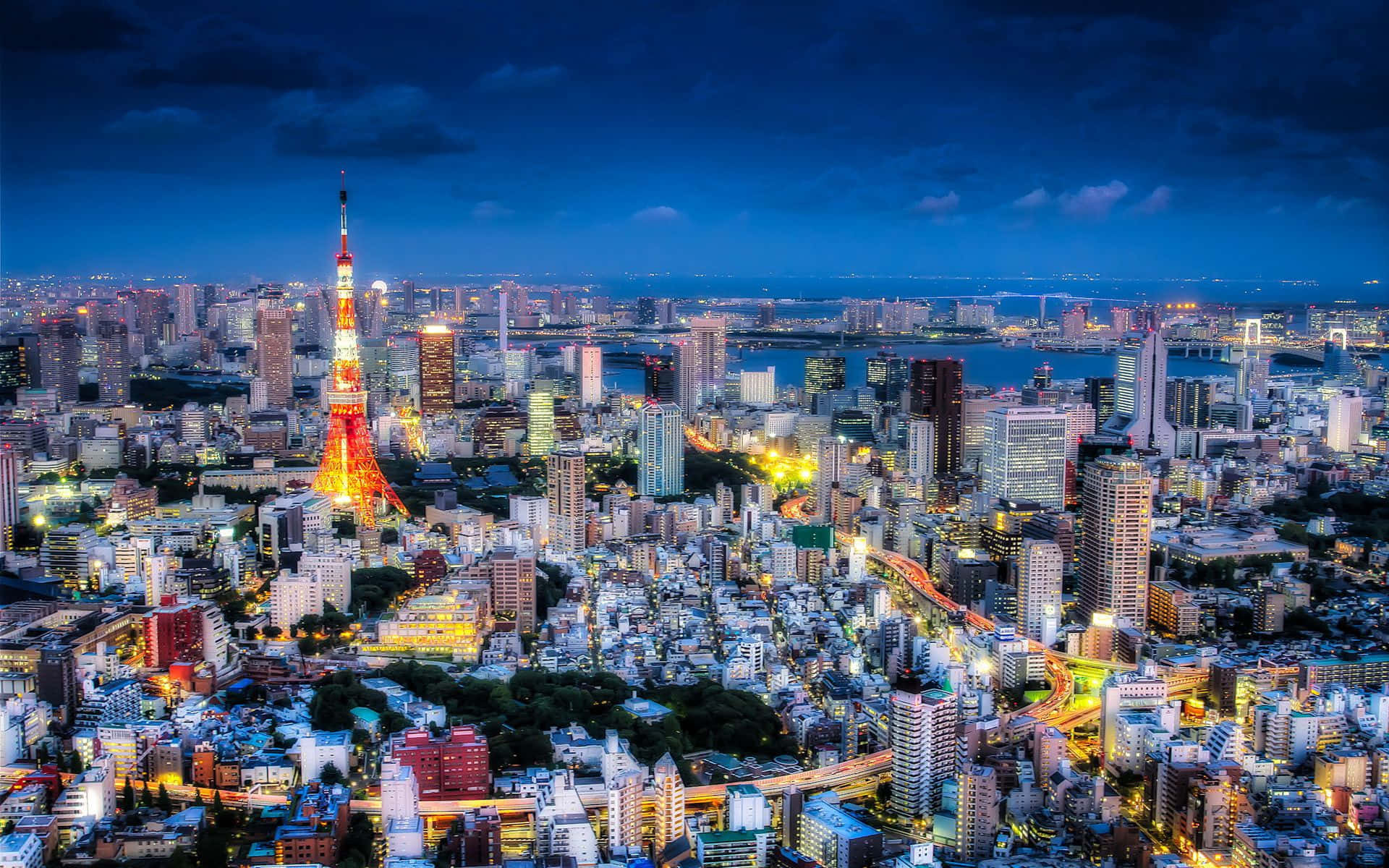 東京 桌布 壁紙 — 黃昏時分的東京天際線，東京塔和城市燈光在深藍色天空下照亮城市景觀。