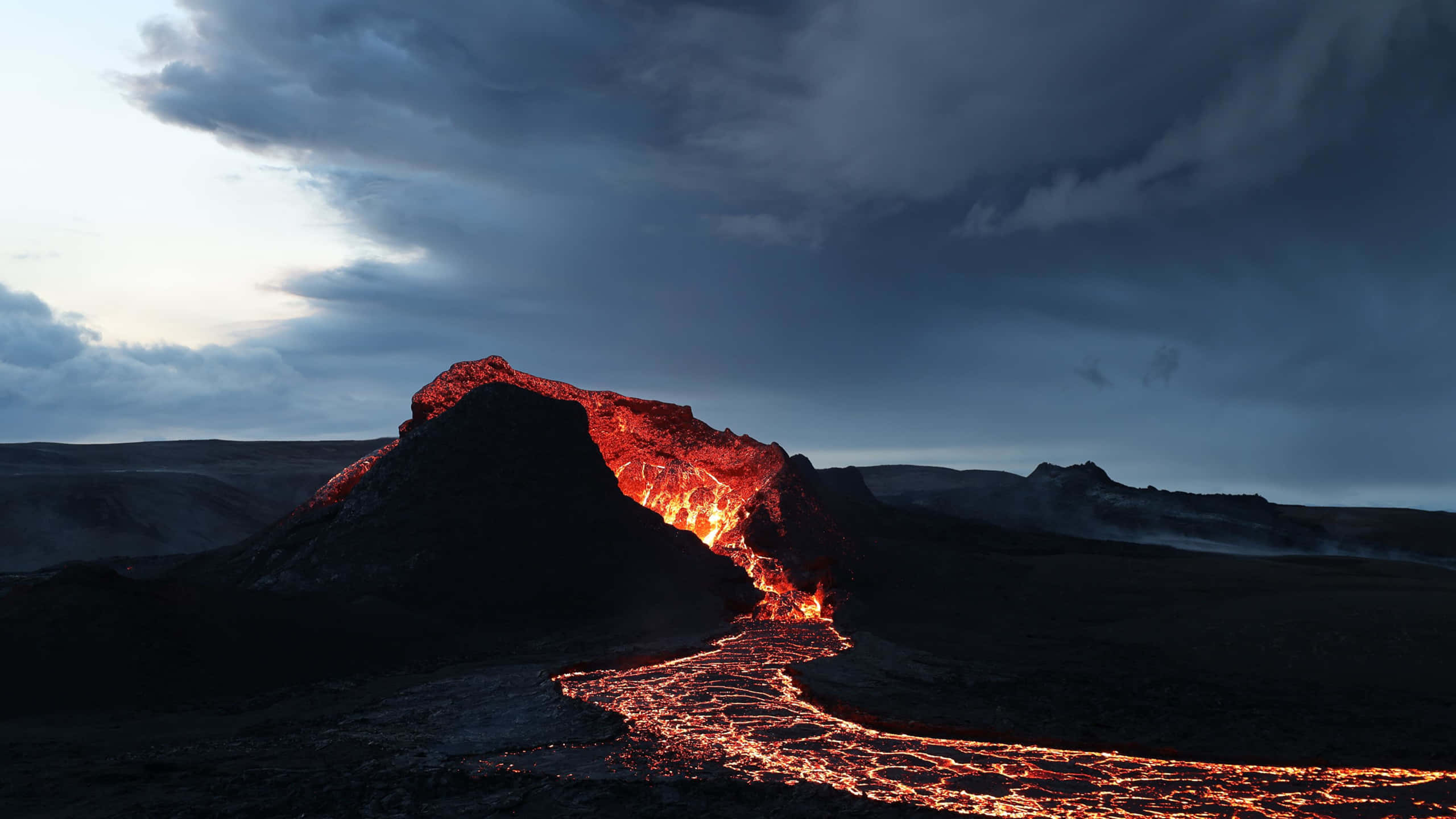 山景 桌布 壁紙 — 黃昏時分的火山爆發，在黑暗的暴風雲下，熾熱的熔岩沿著崎嶇的山脈流下。