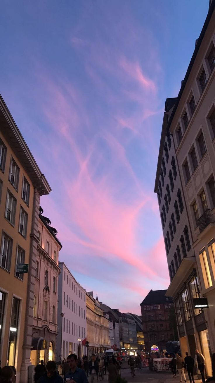 Munich 桌布 壁紙 — 黃昏時分的狹窄歐洲街道，粉彩粉紅和藍色雲彩籠罩在歷史建築和下方行人之上。