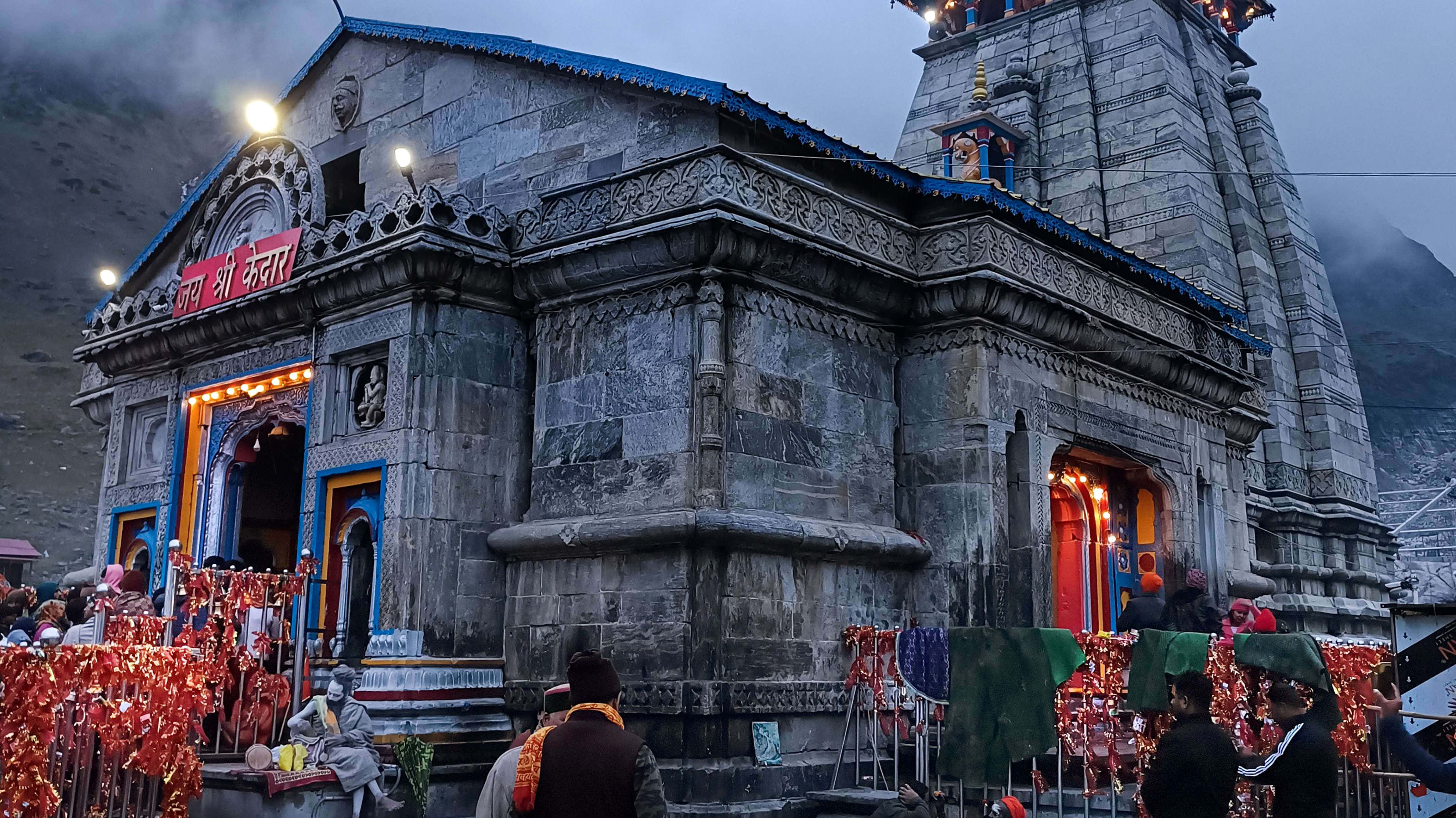 Kedarnath 桌布 壁紙 — 黃昏時分的石廟，紅光閃爍，信徒聚集在霧氣繚繞的山中。