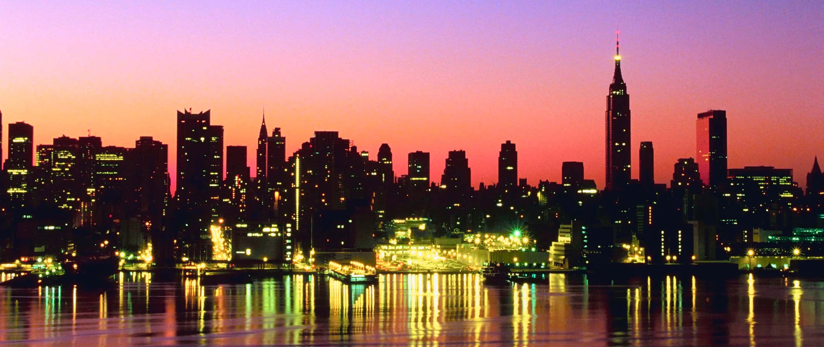 New York City Landscape 桌布 壁紙 — 黃昏時分的紐約市天際線，充滿活力的紫色和橙色天空倒映在下方平靜的水面上。