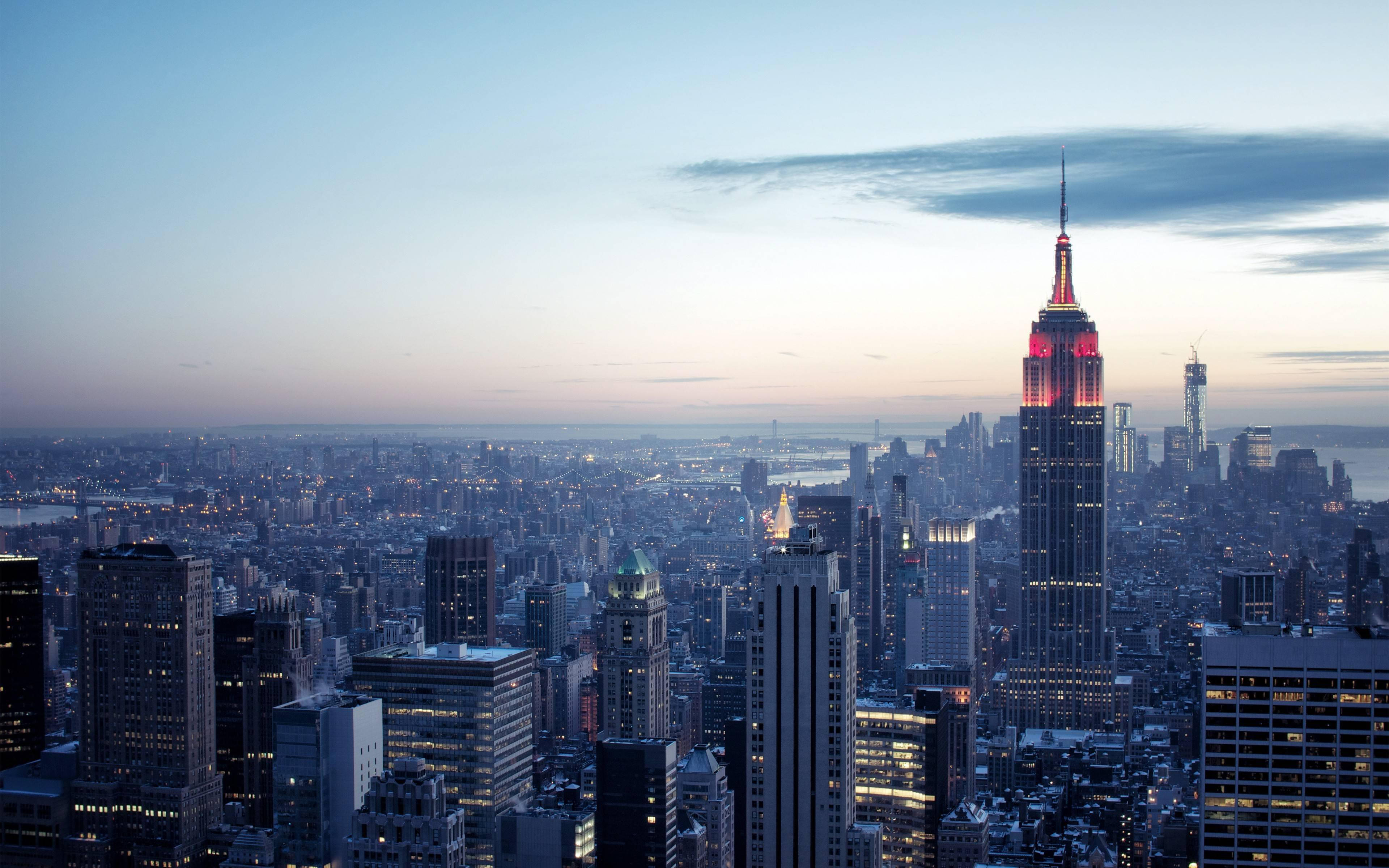 New York 桌布 壁紙 — 黃昏時分的紐約市天際線，帝國大廈在柔和的藍色和橙色天空中閃耀著紅光。