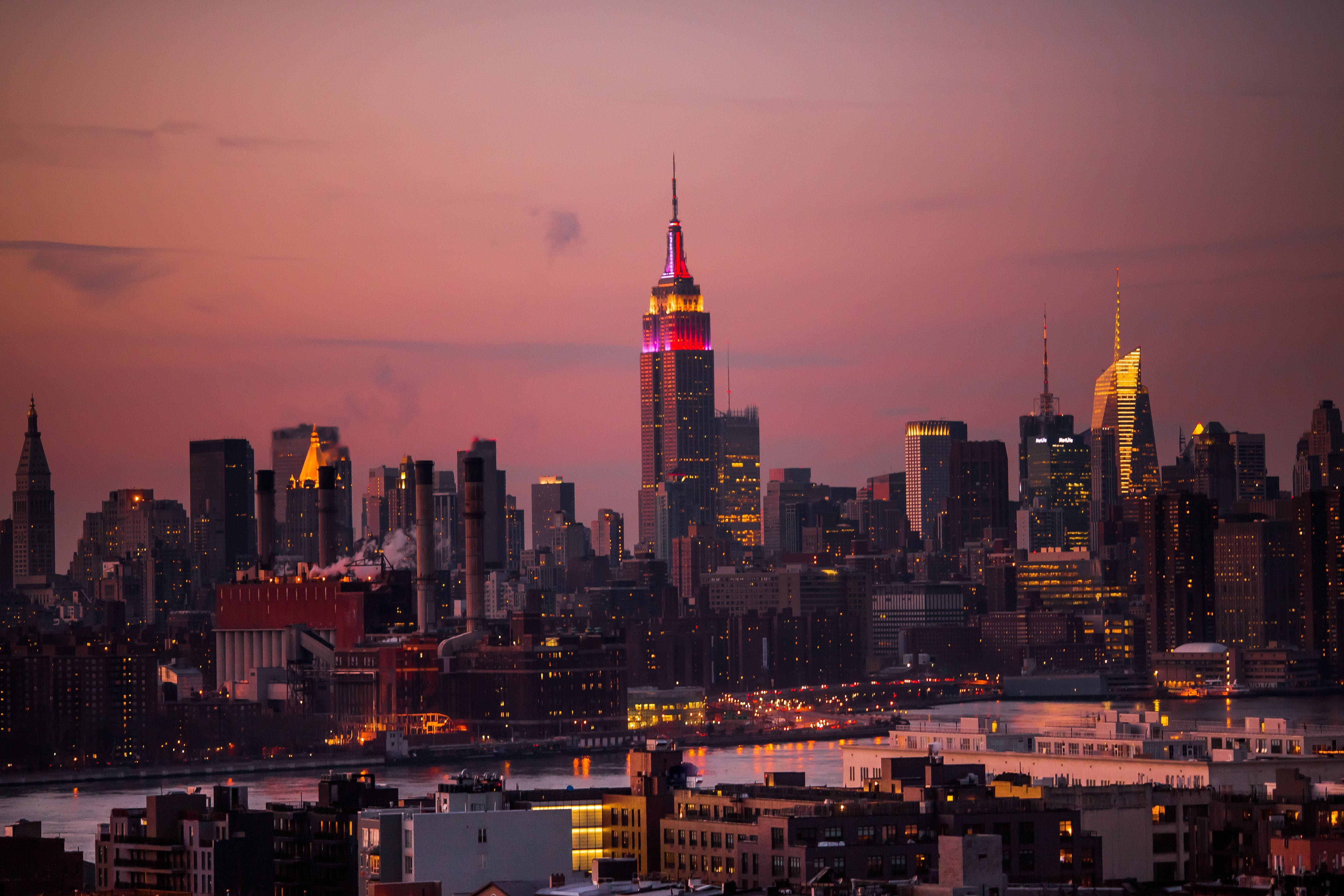 new york 4K 桌布 壁紙 — 黃昏時分的紐約市天際線，帝國大廈在柔和的紫色天空映襯下閃耀著粉紅色和金色光芒。