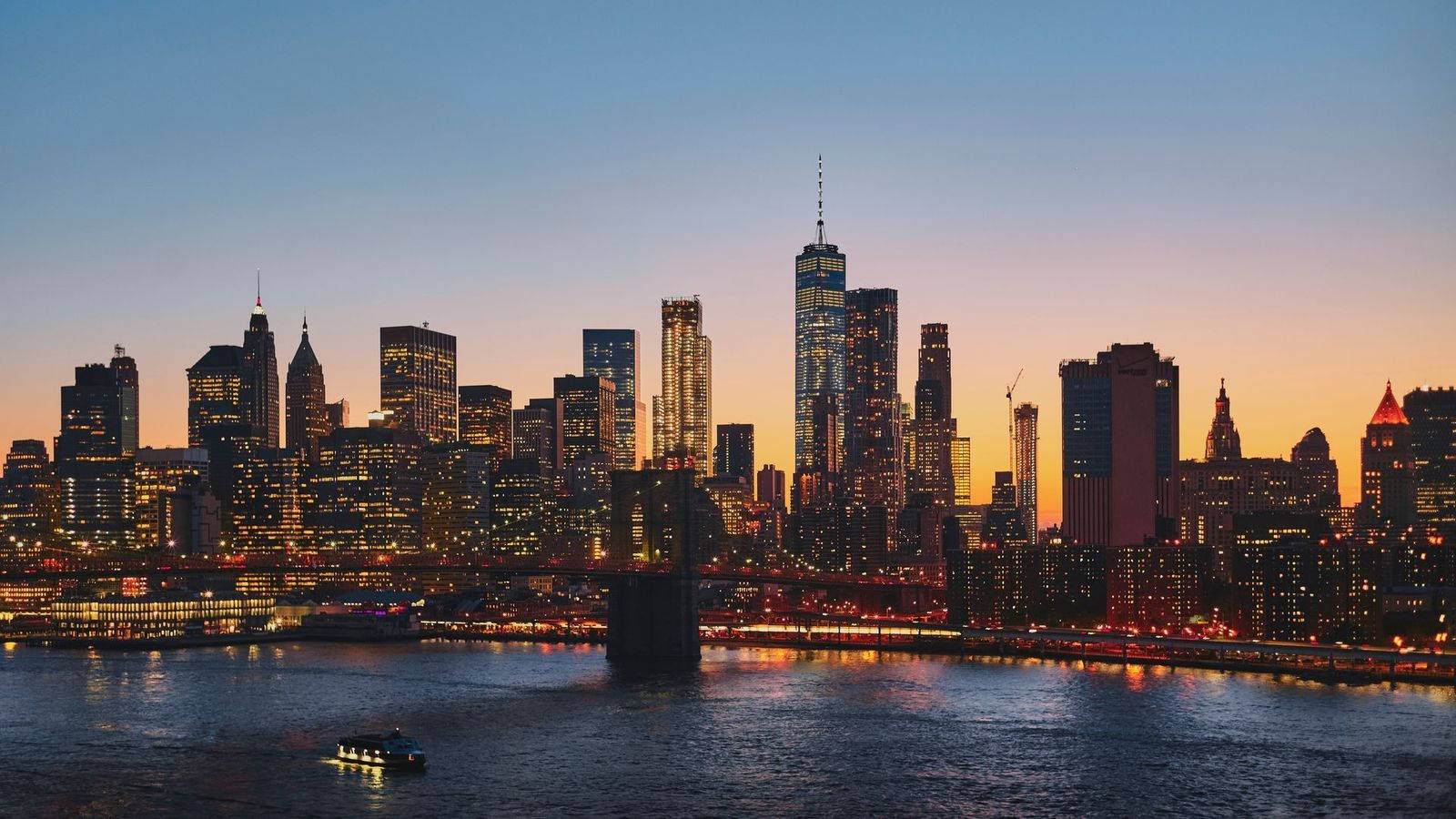Nyc Aesthetic 桌布 壁紙 — 黃昏時分的紐約市天際線，燈火通明的摩天大樓倒映在水面上，一艘船駛過。