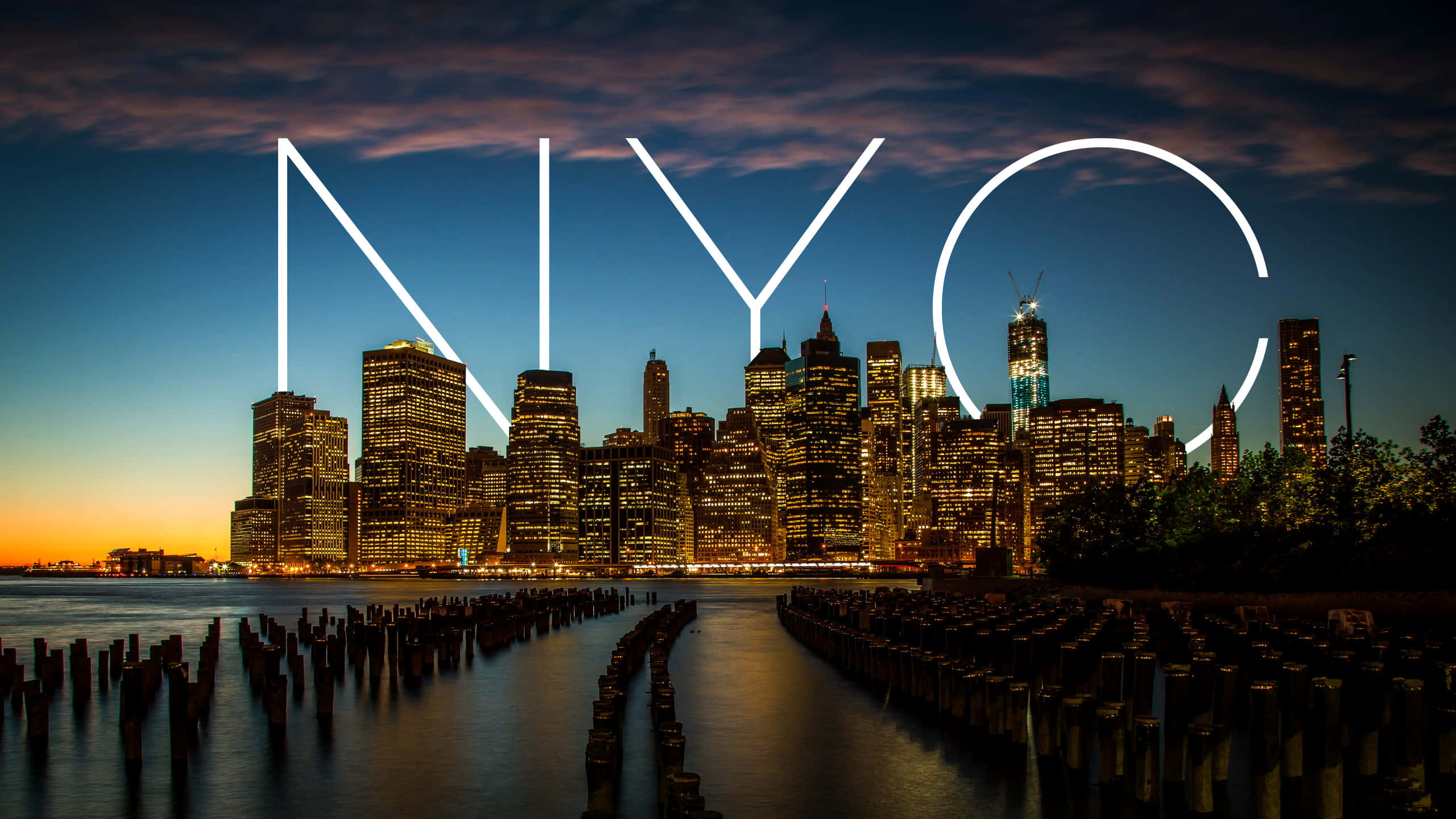 City Desktop 桌布 壁紙 — 黃昏時分的紐約市天際線，發光的「NYC」字母疊加在水面和木樁上。