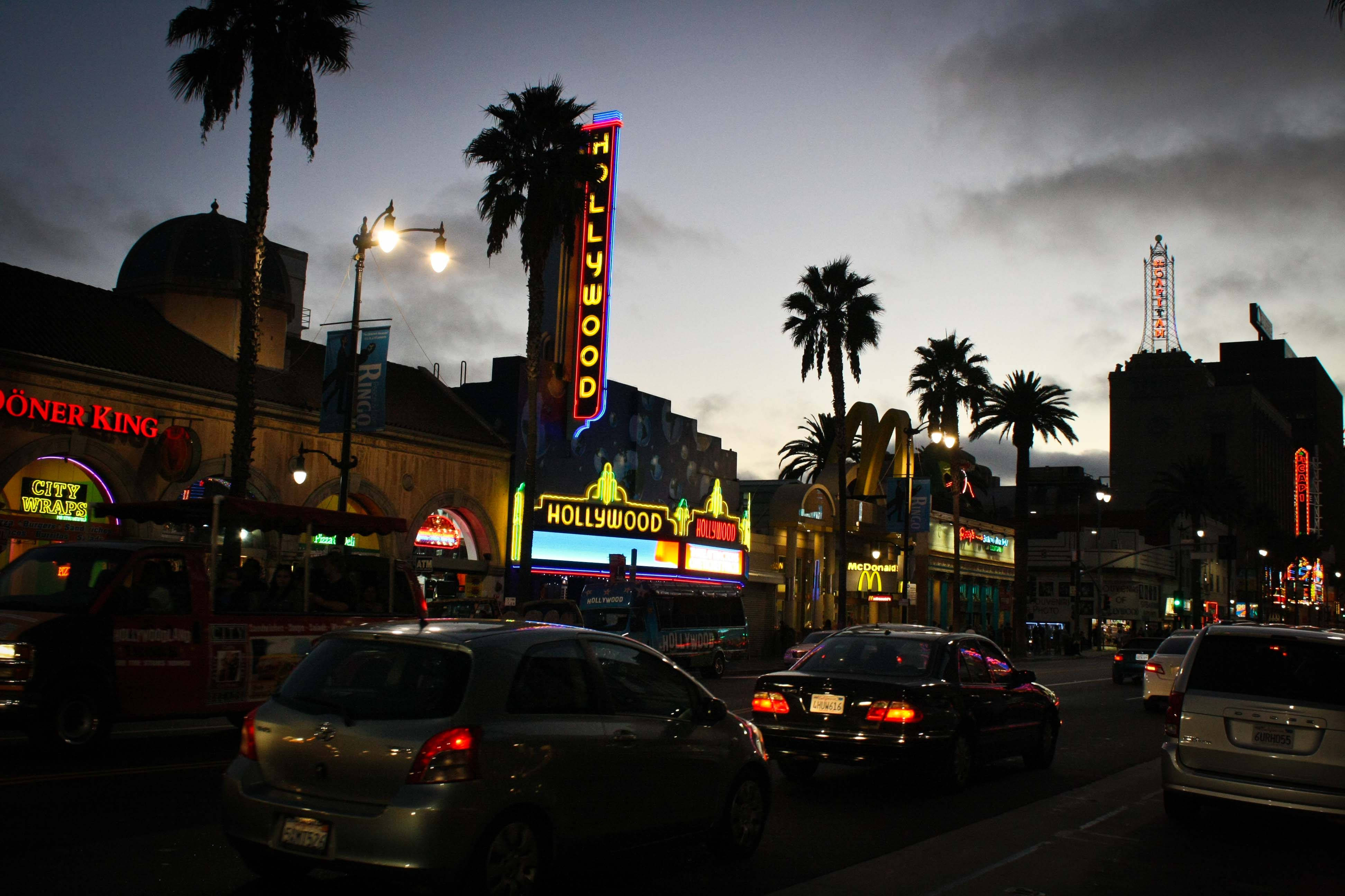 hollywood street 桌布 壁紙 — 黃昏時分的荷里活大道，霓虹燈閃爍，棕櫚樹和汽車在陰雲密布的天空下。