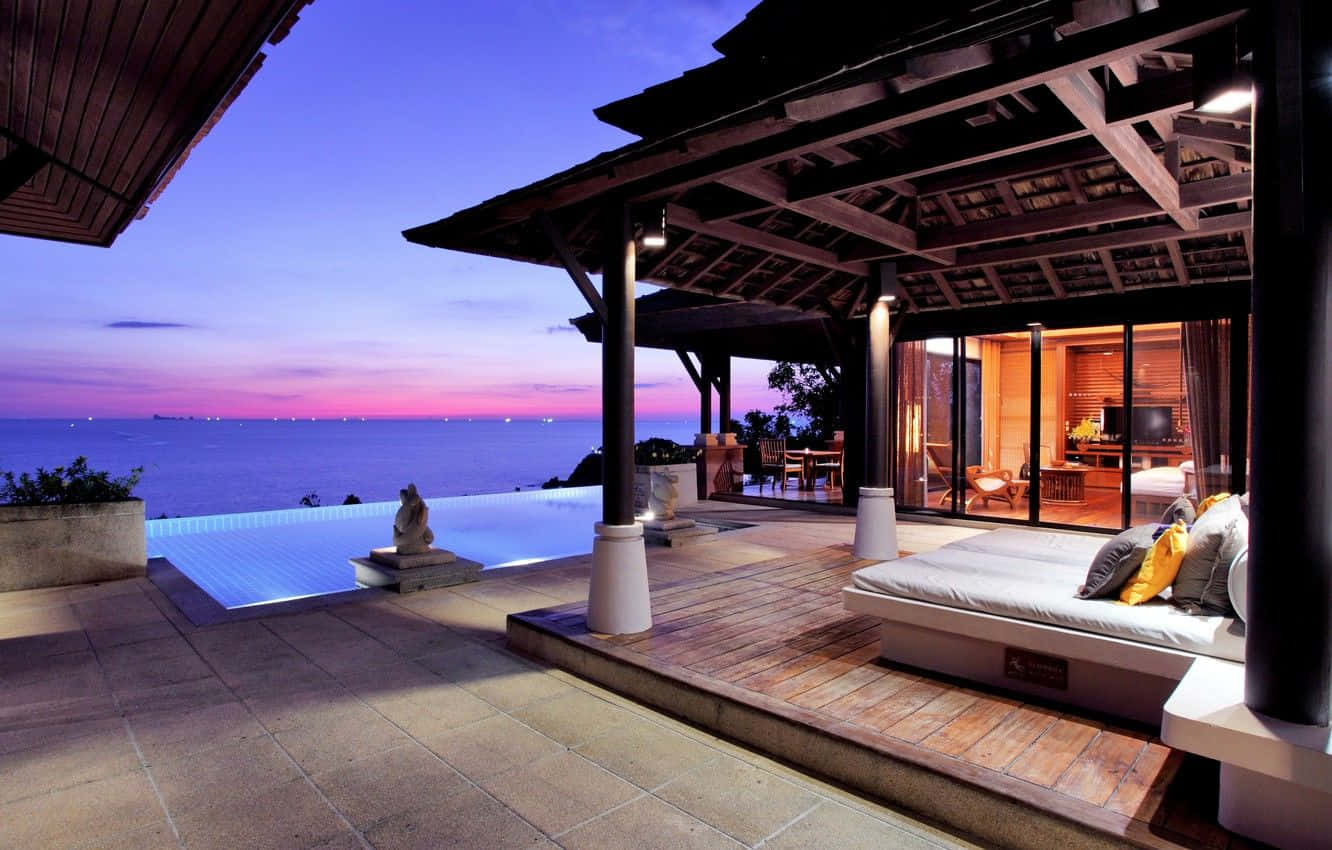 Beach Resort 桌布 壁紙 — 黃昏時分的豪華別墅露台，設有無邊際泳池，俯瞰海洋日落和發光的室內。