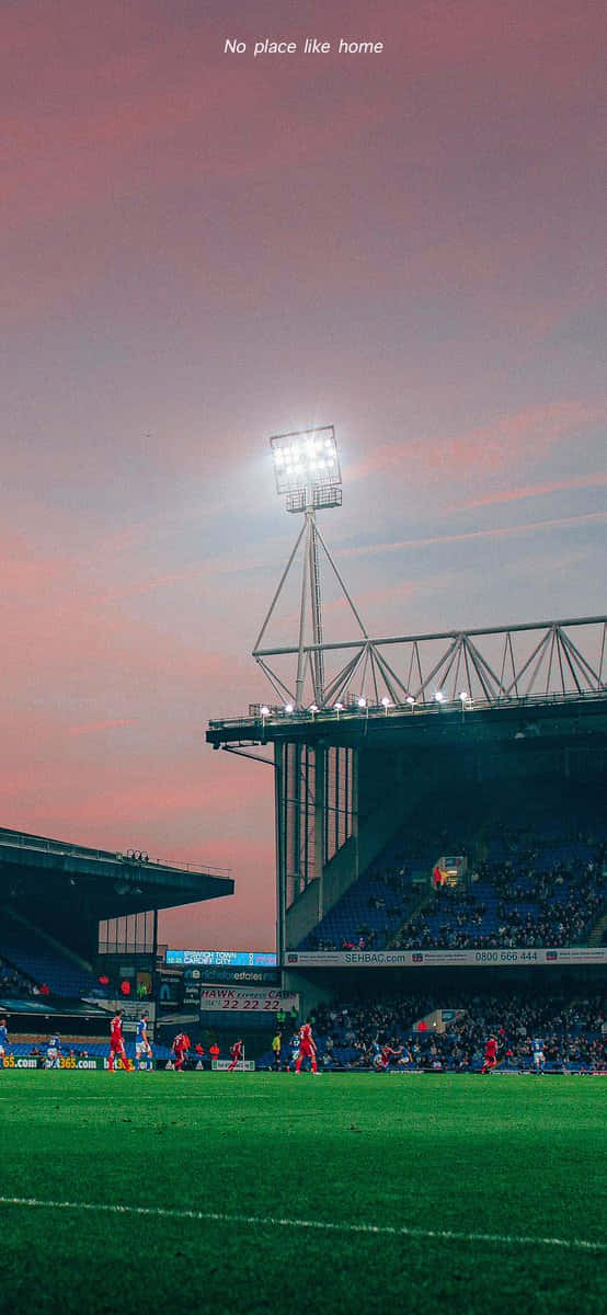 Ipswich Town 桌布 壁紙 — 黃昏時分的足球場，充滿活力的粉紅色天空和發光的泛光燈照亮了綠色球場和藍色座位。
