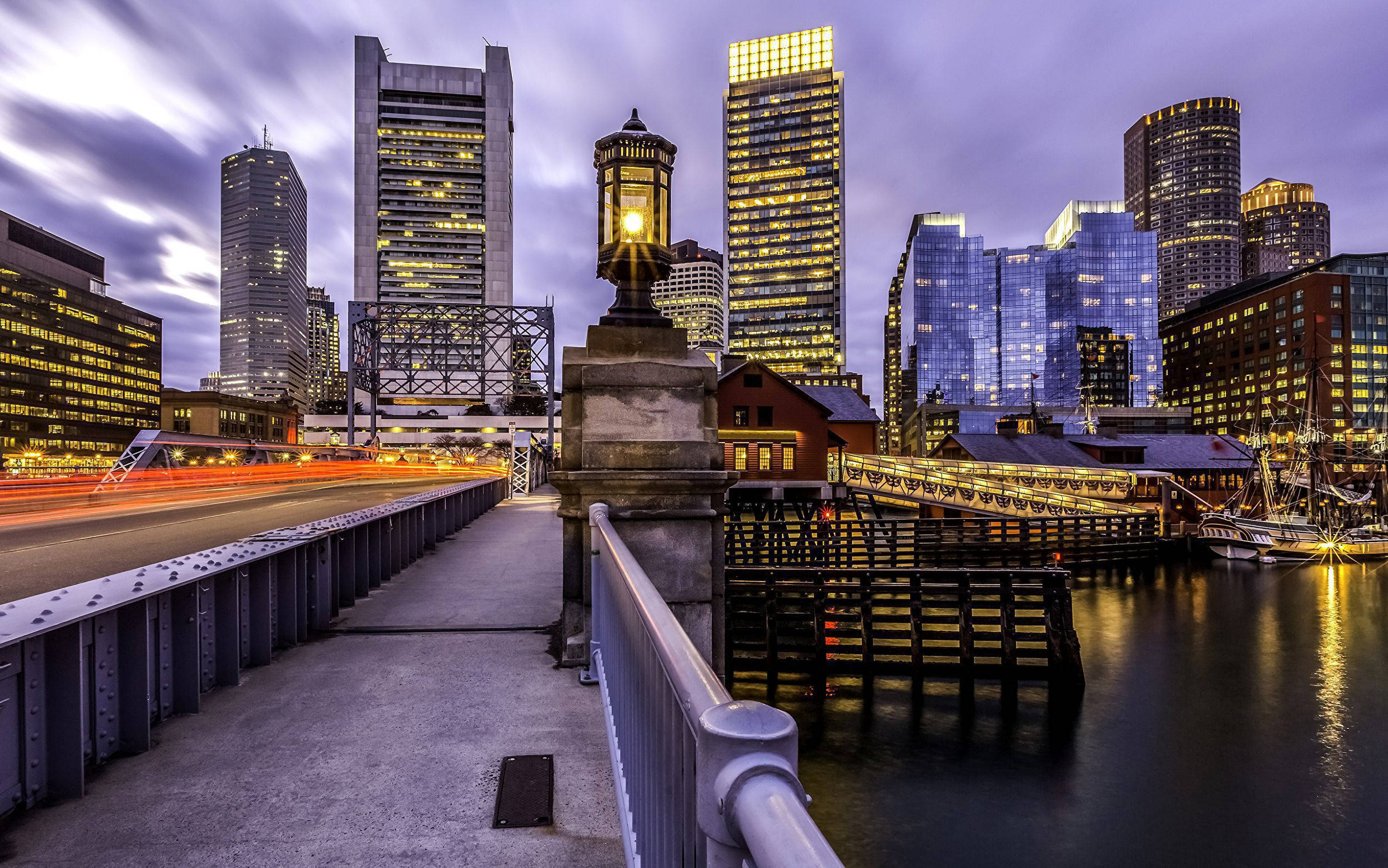 Boston 桌布 壁紙 — 黃昏時分的長時間曝光城市景觀，發光的摩天大樓倒映在水面上，車流燈光形成條紋。