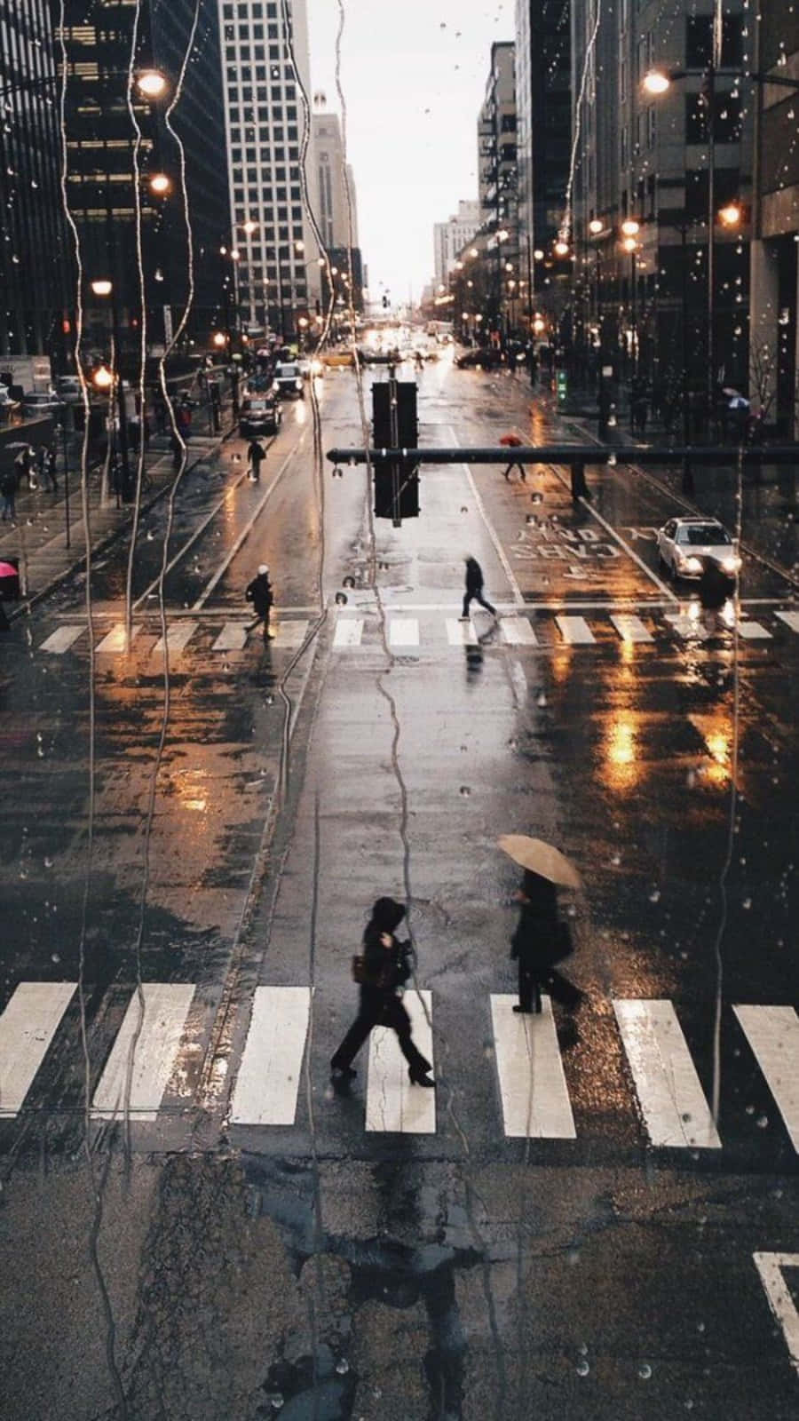 Rainy Day 桌布 壁紙 — 黃昏時分的雨城市街道，行人在濕漉漉的斑馬線上穿行，下方是發光的街燈和高樓大廈。