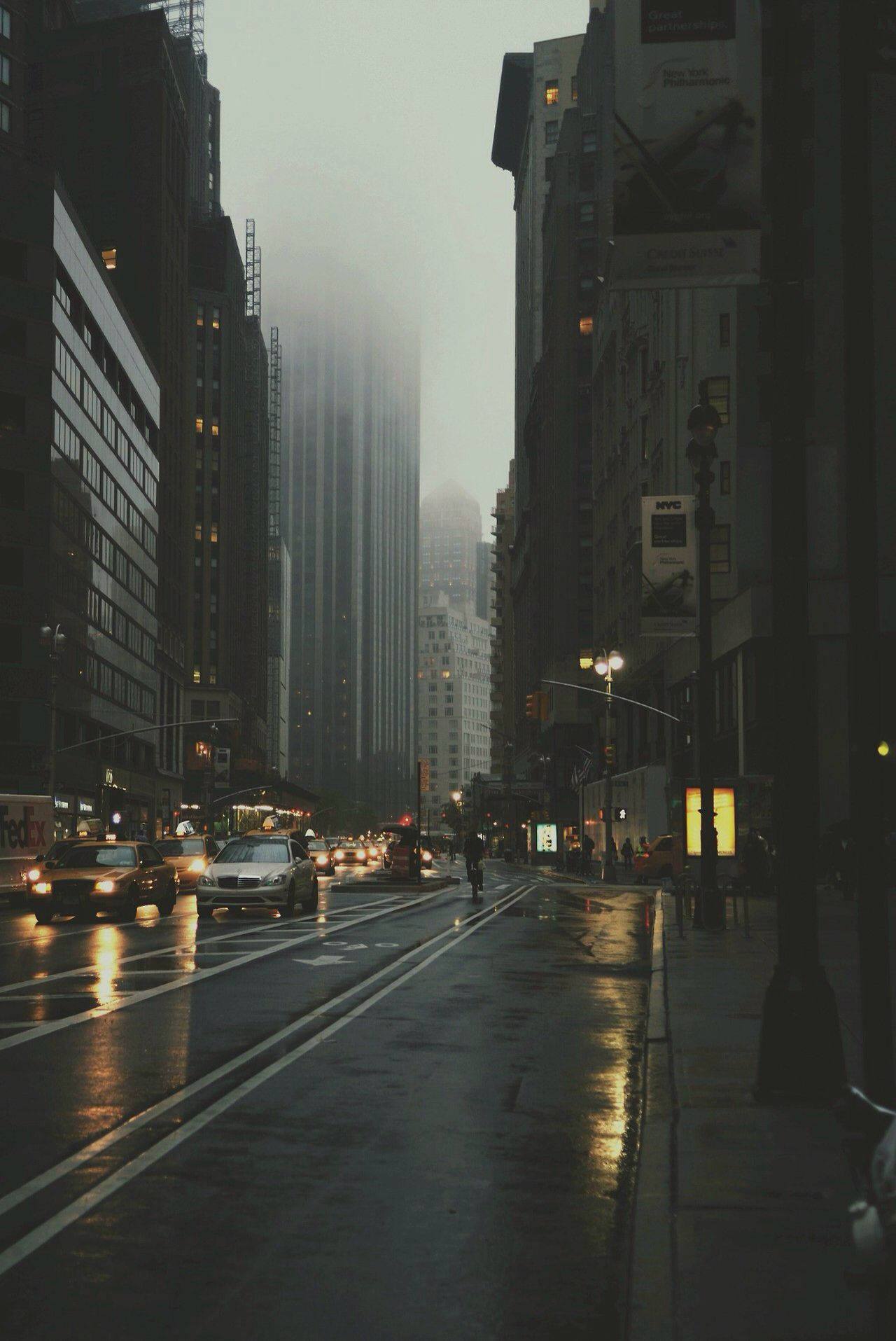 Screen 桌布 壁紙 — 黃昏時分的雨街，濕漉漉的路面反射著車燈，高聳的建築物籠罩在霧中。