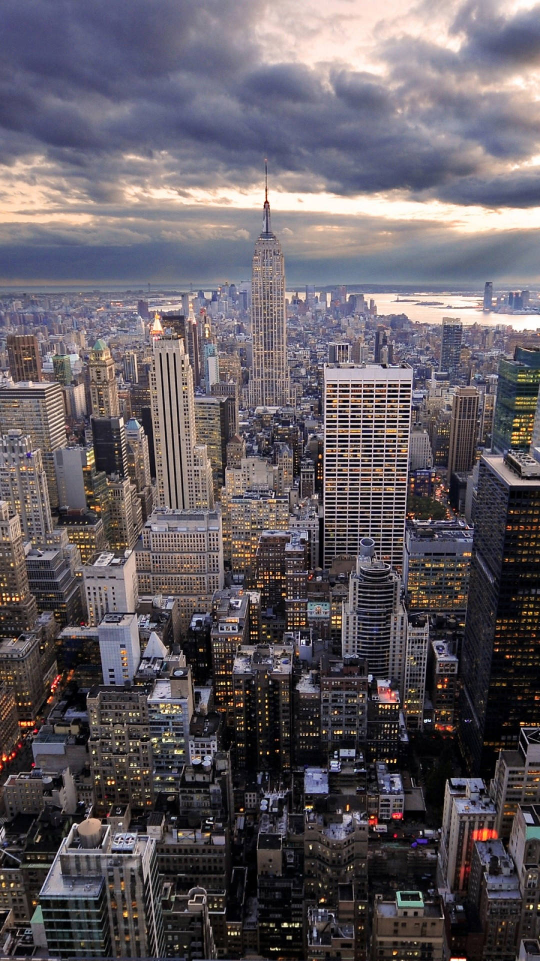 new york city iPhone x 桌布 壁紙 — 黃昏時分紐約市天際線的戲劇性航拍，帝國大廈在暴風雲下高聳入雲。