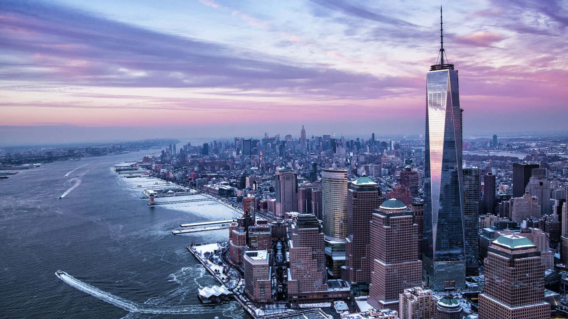 New York 桌布 壁紙 — 黃昏時分紐約市天際線的鳥瞰圖，世界貿易中心一號樓在積雪的建築物和河面上反射出粉紅色和紫色的雲彩。
