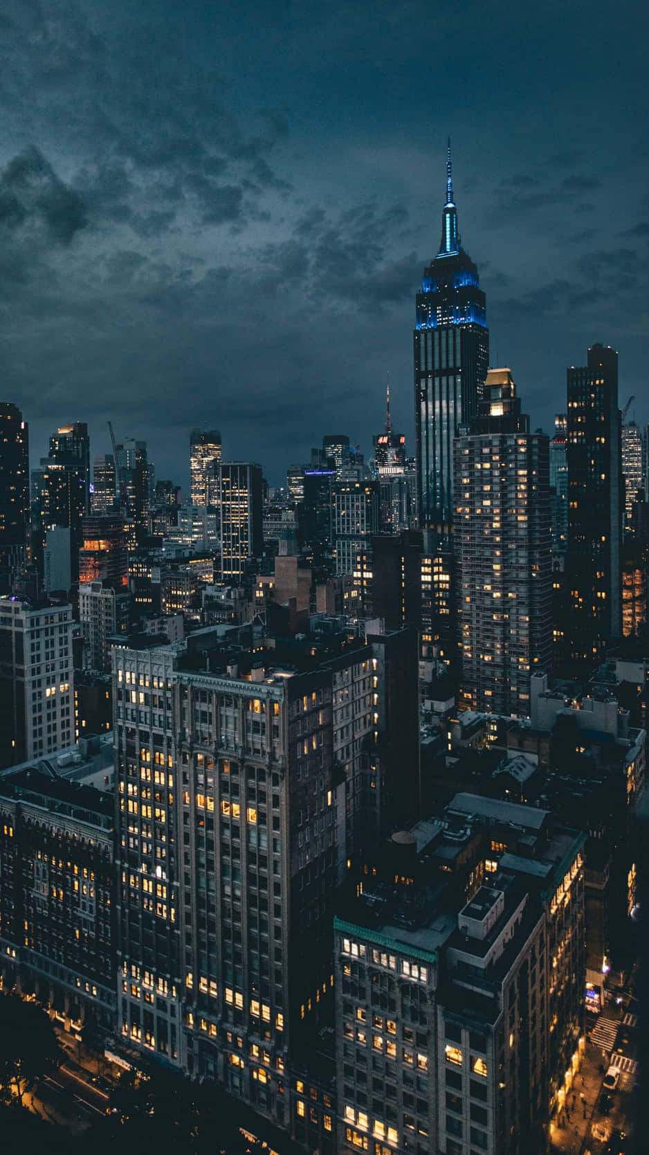 Buildings 桌布 壁紙 — 黃昏時分紐約市天際線的鳥瞰圖，帝國大廈在烏雲中發出藍色光芒。