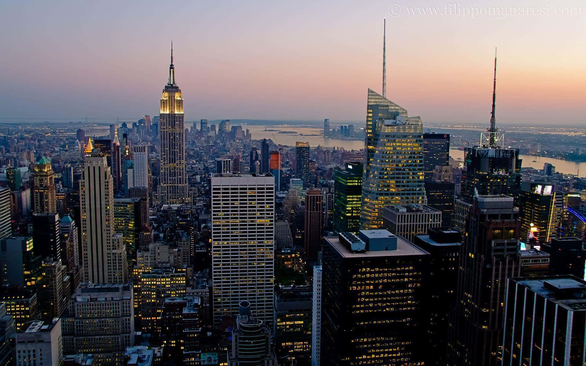 New York 桌布 壁紙 — 黃昏時分紐約市天際線的鳥瞰圖，帝國大廈在粉紅色和紫色的天空映襯下亮起燈光。
