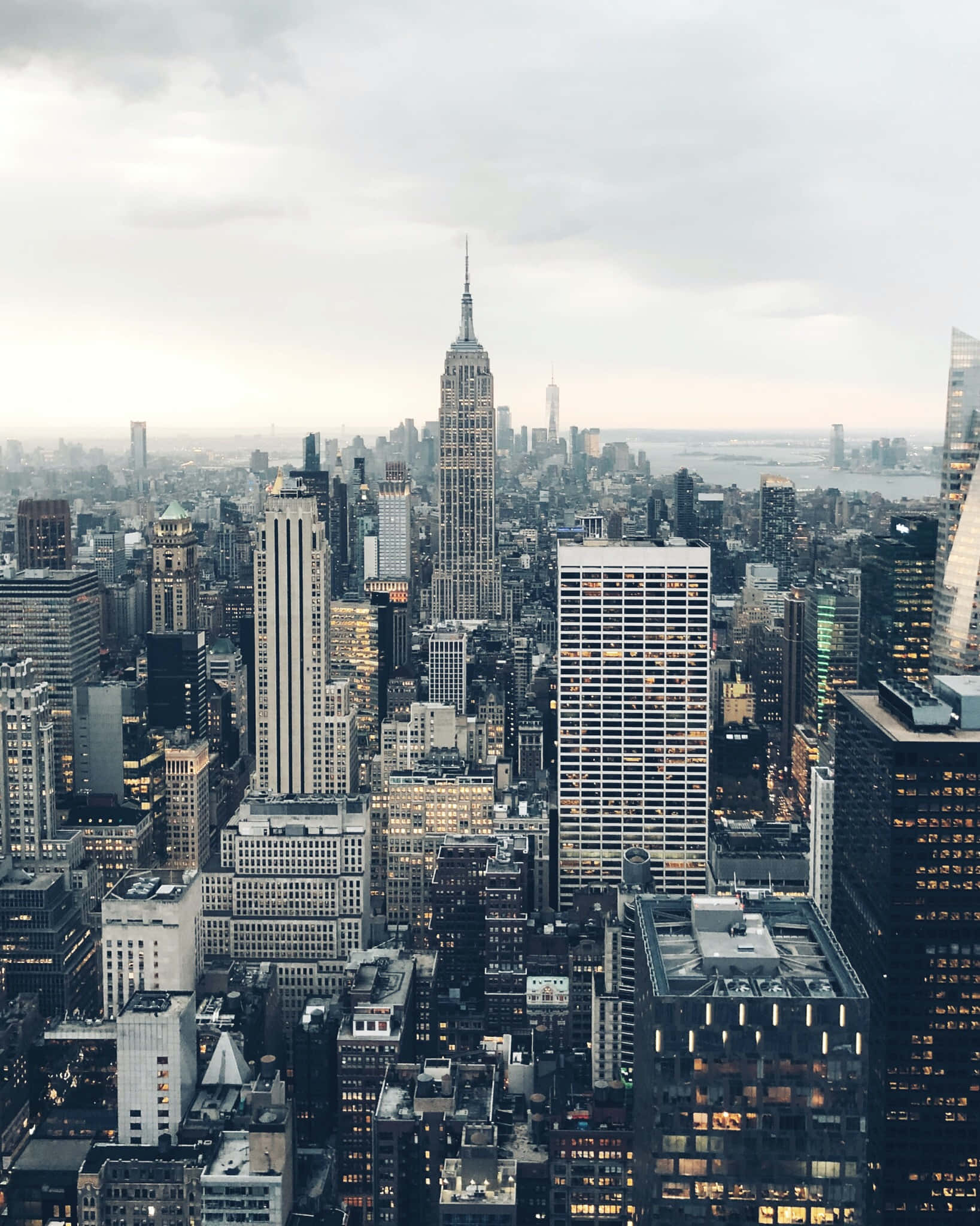 Empire State Building 桌布 壁紙 — 黃昏時分紐約市天際線的鳥瞰圖，帝國大廈在陰雲密布的天空下聳立於密集的摩天大樓之上。