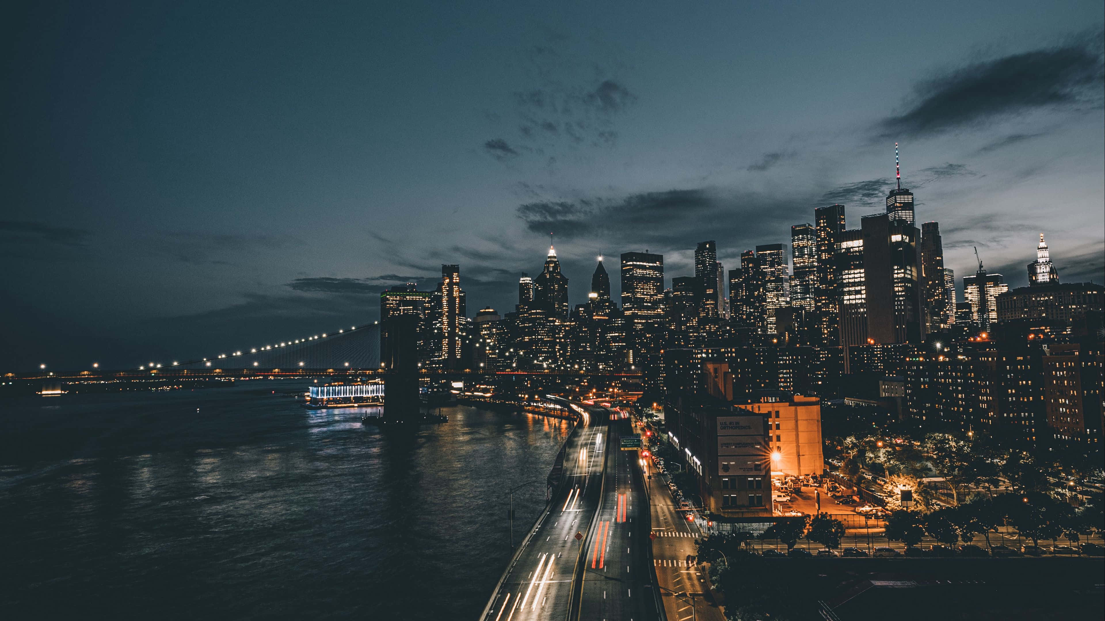 夜景城市 桌布 壁紙 — 黃昏時分紐約市天際線的鳥瞰圖，有燈火通明的摩天大樓和海濱道路上的車流光軌。