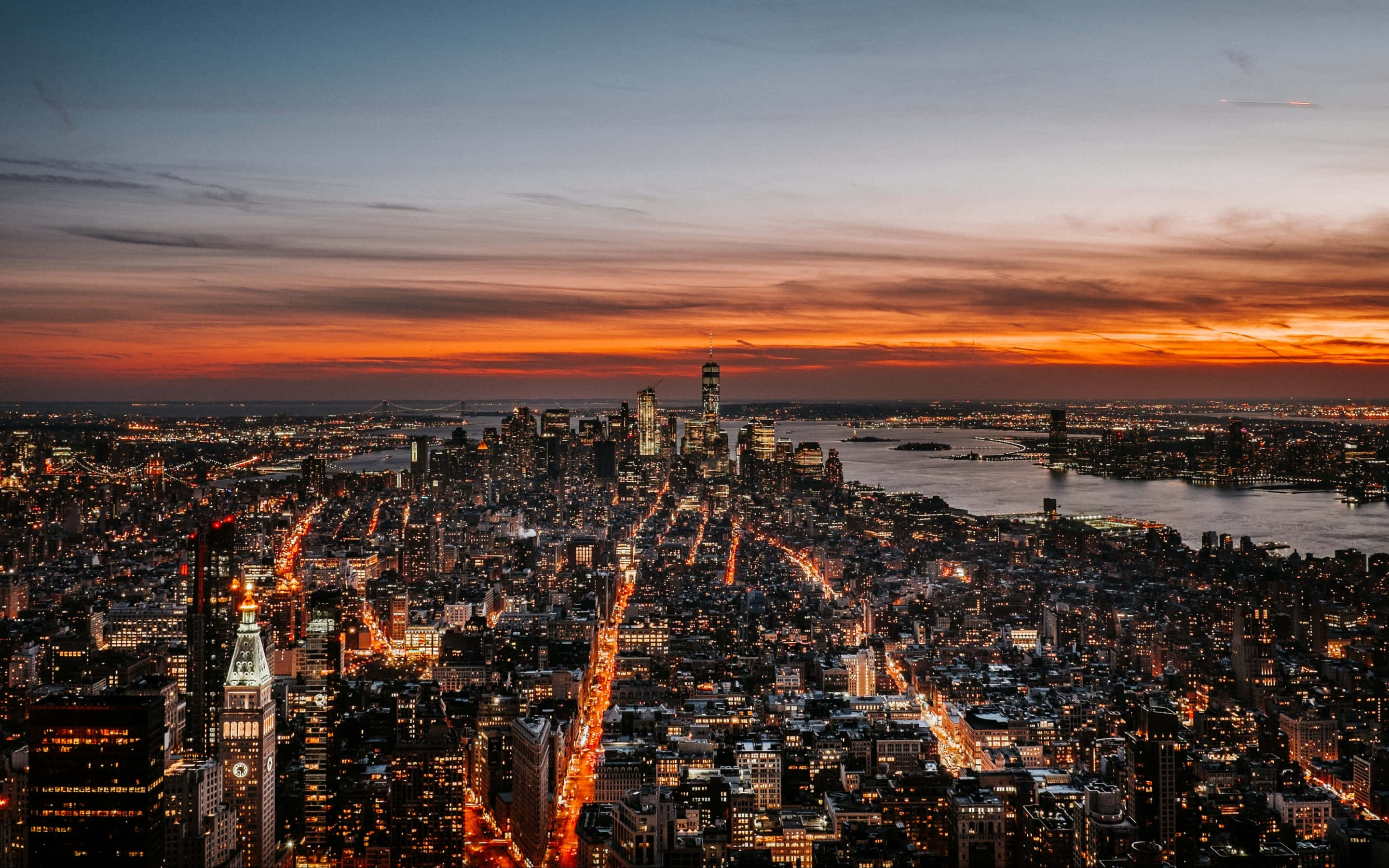 New York City 4K Ultra HD 桌布 壁紙 — 黃昏時分紐約市天際線的鳥瞰圖，火紅的橙色夕陽和閃爍的路燈照亮了密集的城市擴展區。
