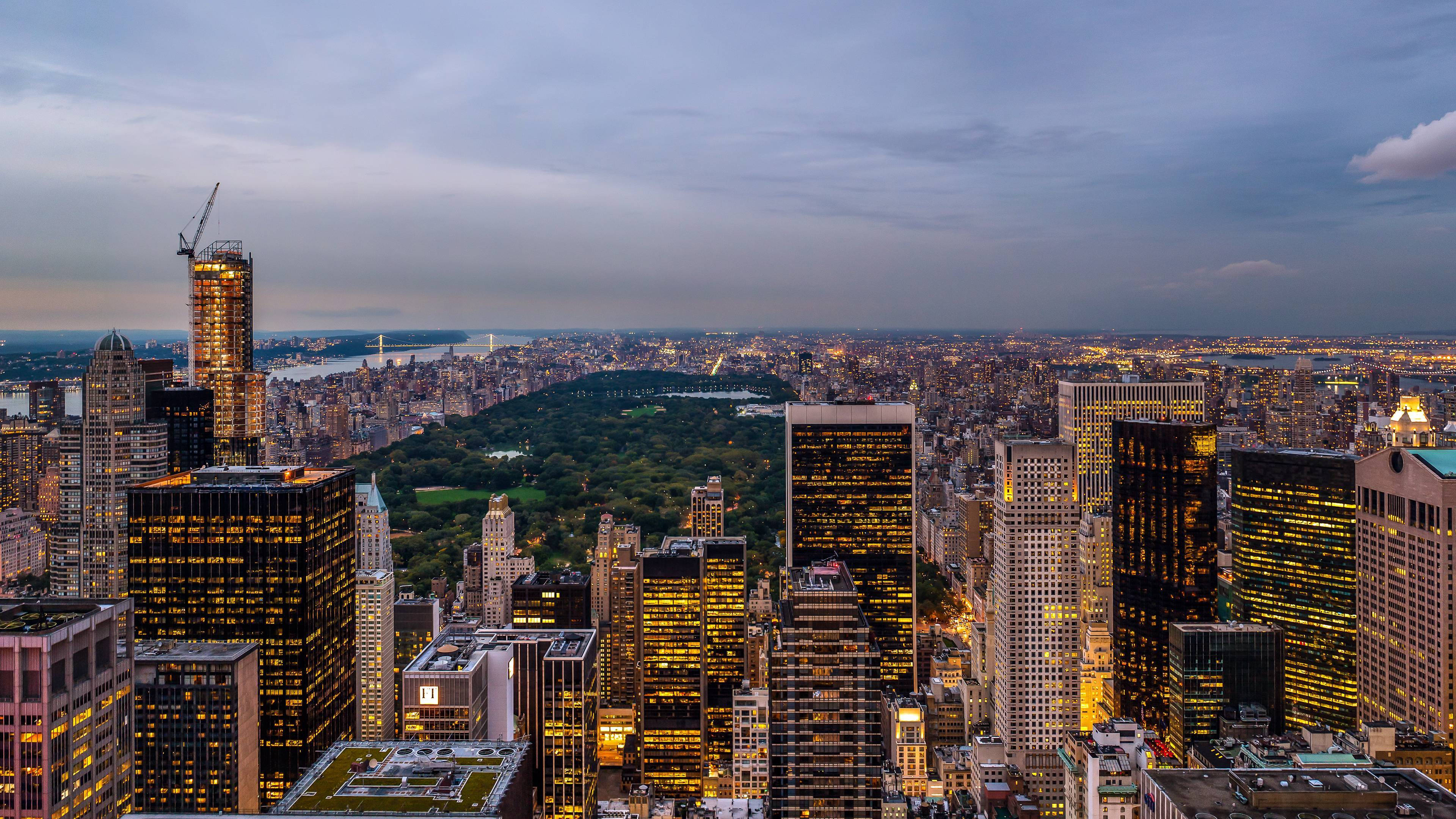 4K New York City 桌布 壁紙 — 黃昏時分紐約市的全景，中央公園在金色窗戶照亮的摩天大樓中閃爍著綠光。