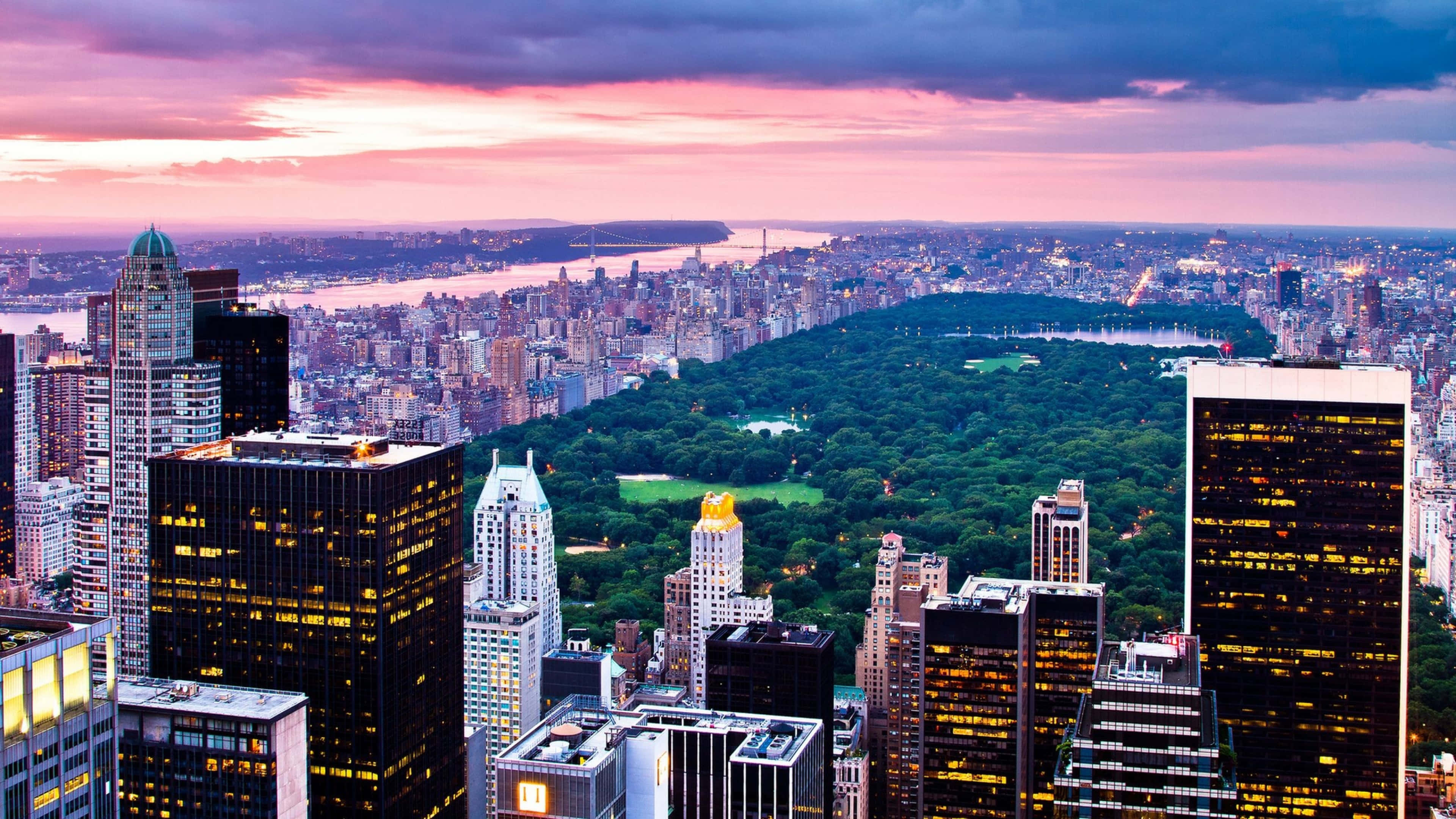 New York City 4K Ultra HD 桌布 壁紙 — 黃昏時分紐約市的鳥瞰圖，中央公園在粉紅色和紫色的天空下，在摩天大樓中閃爍著綠色光芒。