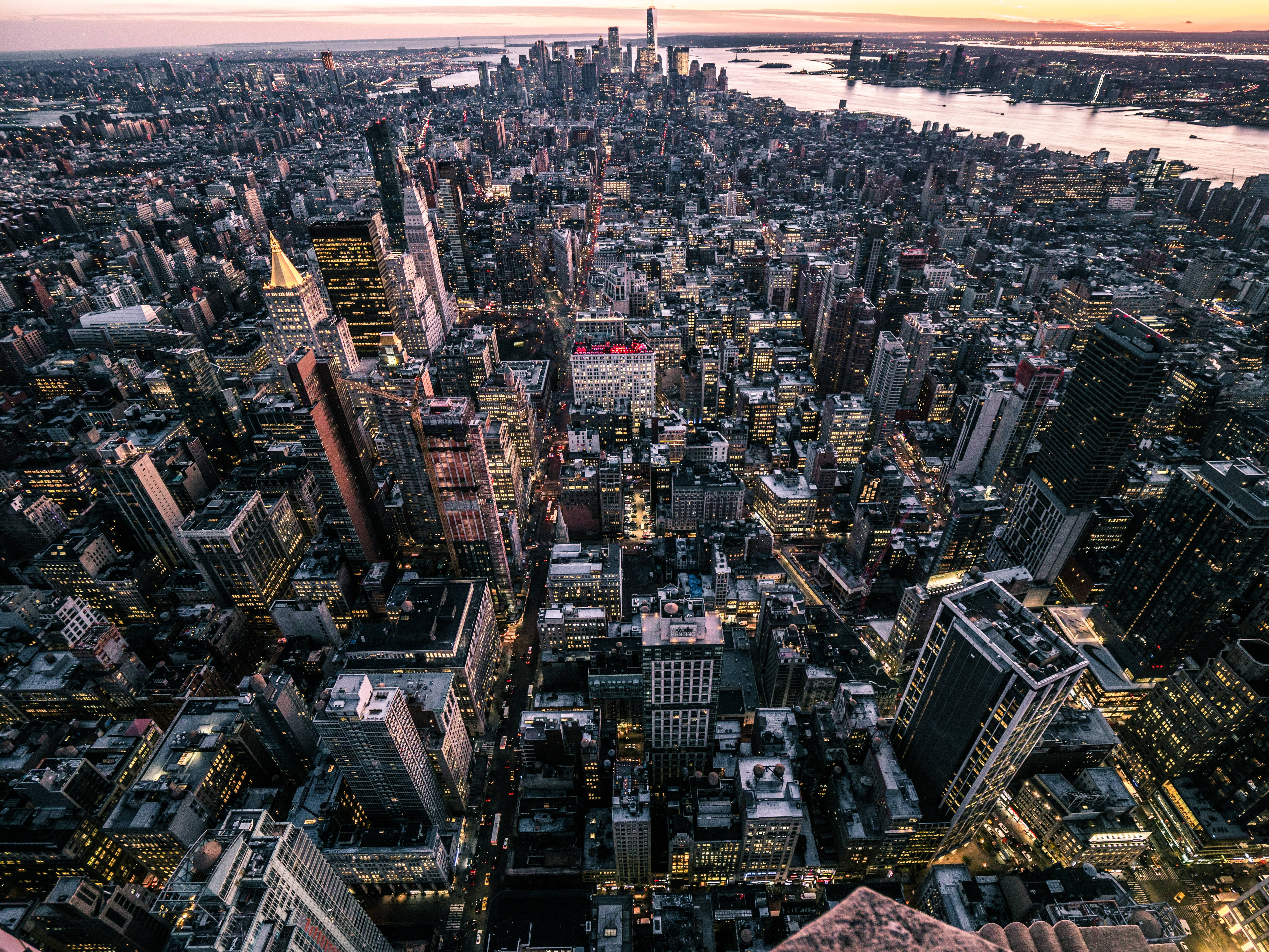 New York 桌布 壁紙 — 黃昏時分紐約市的鳥瞰圖，閃爍的摩天大樓和河流映照著逐漸褪色的橙色天空。