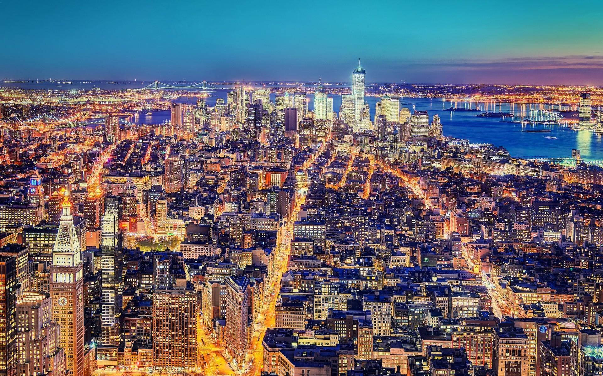 manhattan 桌布 壁紙 — 黃昏時分紐約市的鳥瞰圖，閃爍的摩天大樓和燈火通明的街道倒映在水面上。