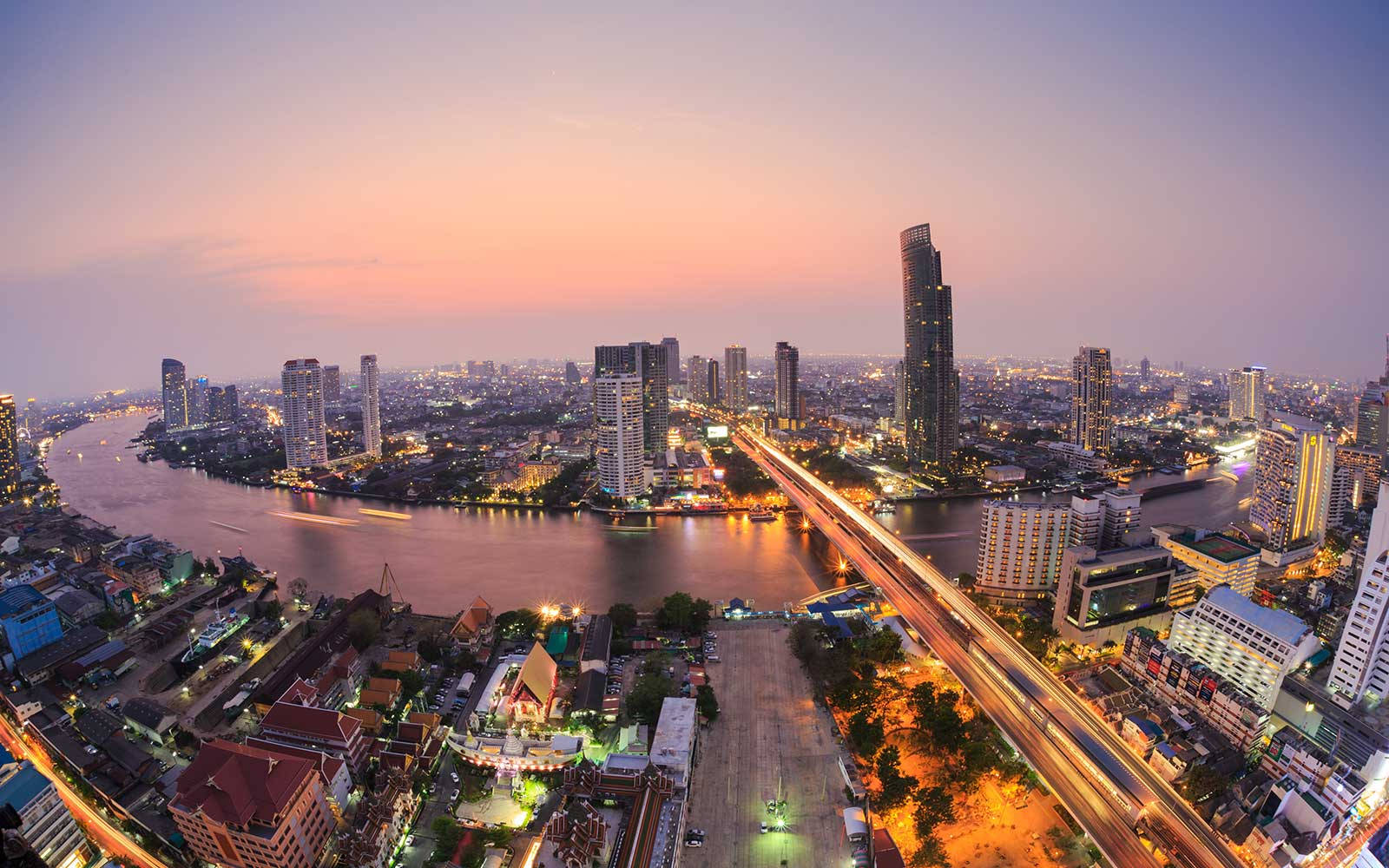Asia 桌布 壁紙 — 黃昏時分繁忙城市景觀的鳥瞰圖，有發光的河流和橋上交通的光跡。