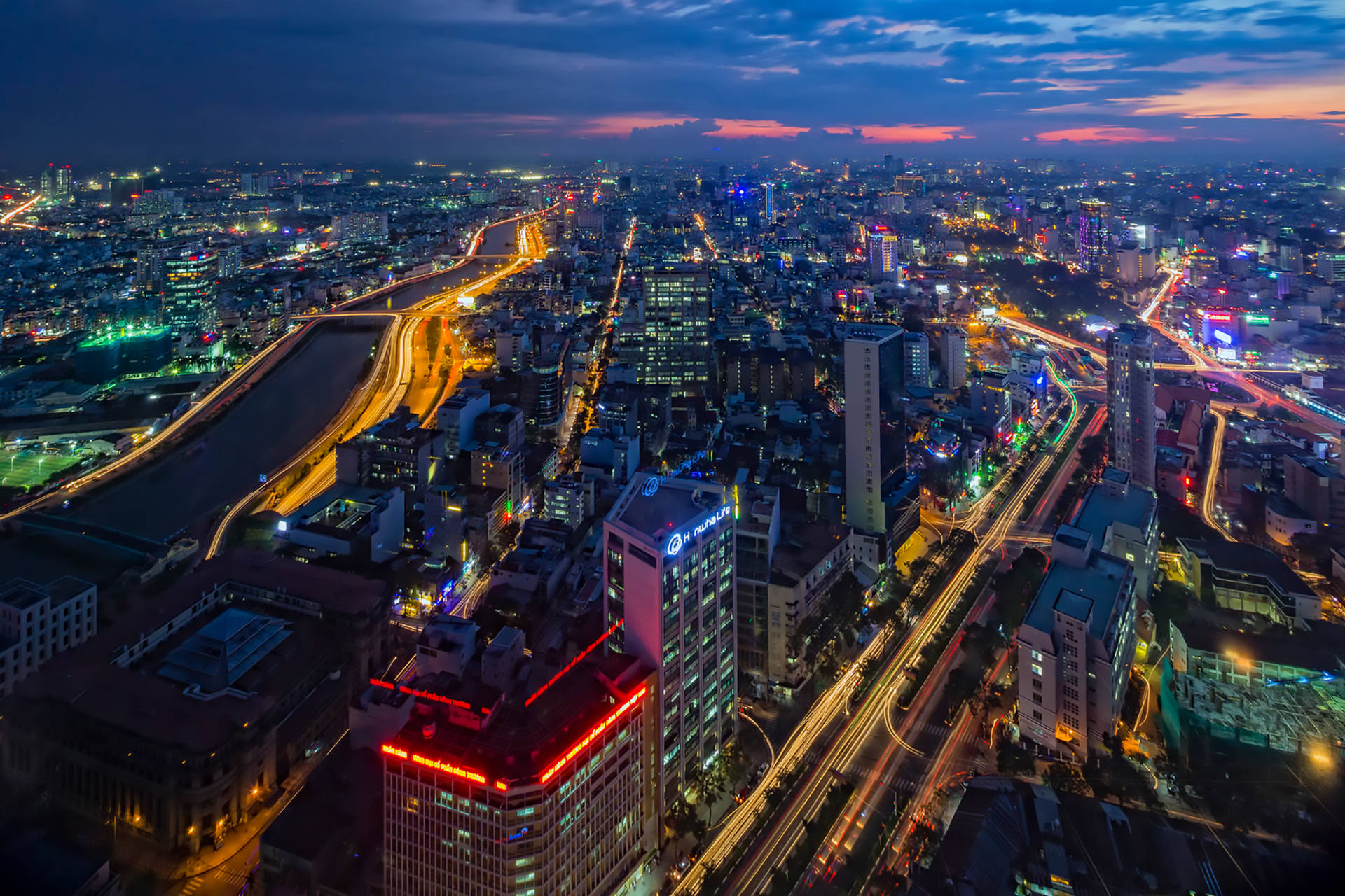 Vietnam 桌布 壁紙 — 黃昏時分繁忙城市的鳥瞰圖，霓虹燈閃爍，車流光軌照亮城市擴展區。