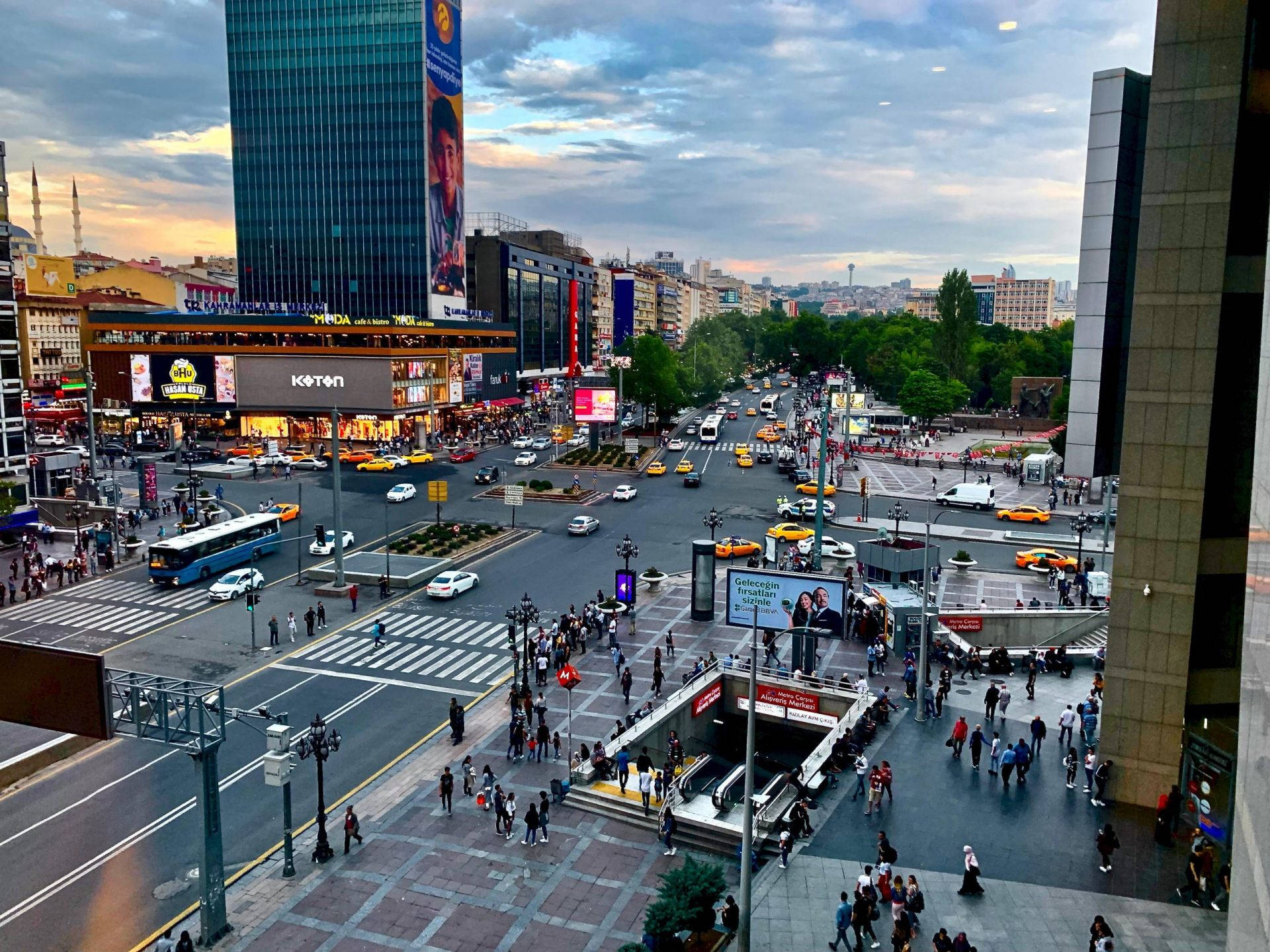 Ankara 桌布 壁紙 — 黃昏時分繁忙的城市十字路口，人群穿梭於滿是黃色計程車和現代高樓大廈的街道，天空多雲。