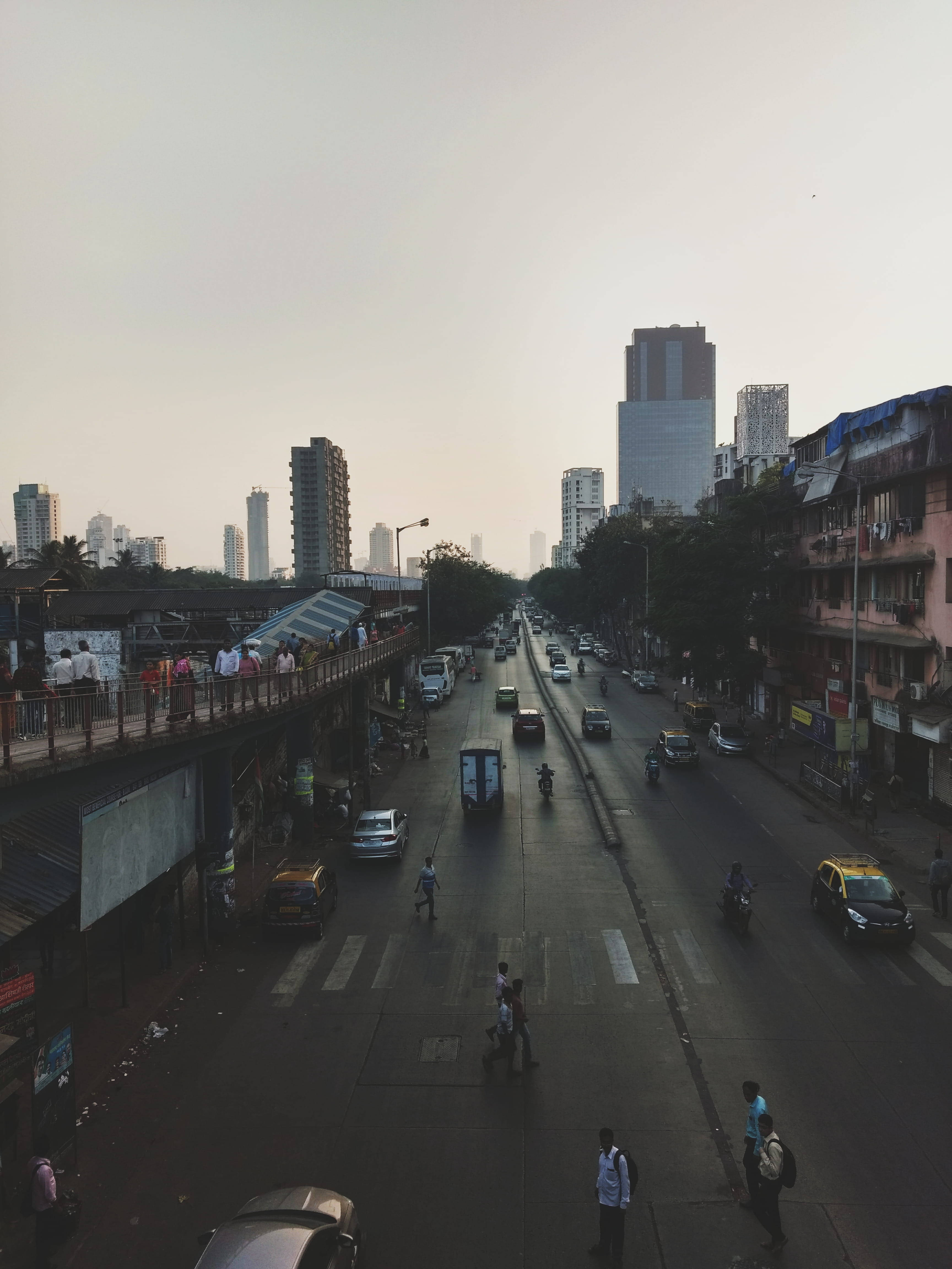 Mumbai 桌布 壁紙 — 黃昏時分繁忙的城市街道，行人過馬路，車輛行駛，高樓大廈在朦朧的天空下聳立。