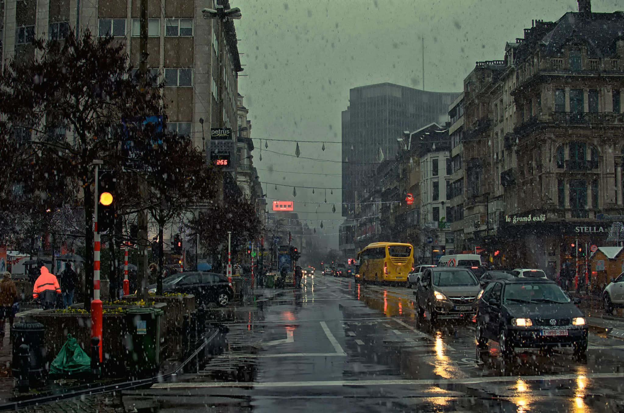Raining 桌布 壁紙 — 黃昏時分被雨淋濕的城市街道，閃爍的交通燈，以及一輛黃色巴士在歷史建築之間的濕滑路面上行駛。