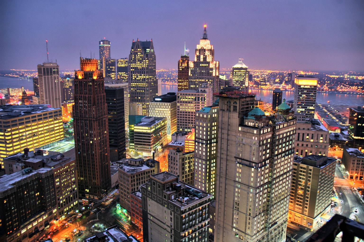detroit 桌布 壁紙 — 黃昏時分被雪覆蓋的城市天際線鳥瞰圖，下方有燈火通明的摩天大樓和發光的河流。