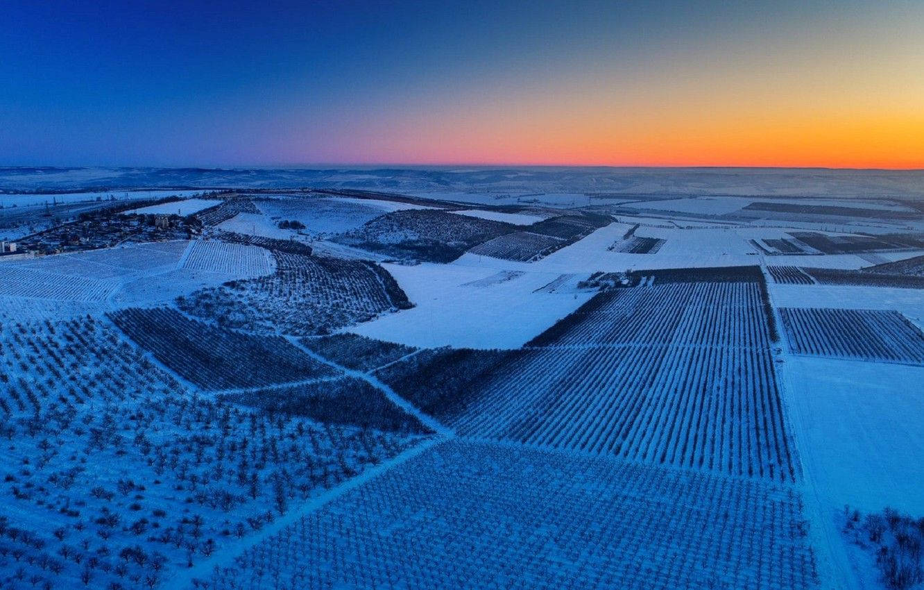 Moldova 桌布 壁紙 — 黃昏時分被雪覆蓋的葡萄園的鳥瞰圖，充滿活力的橙色地平線逐漸融入深藍色的天空。