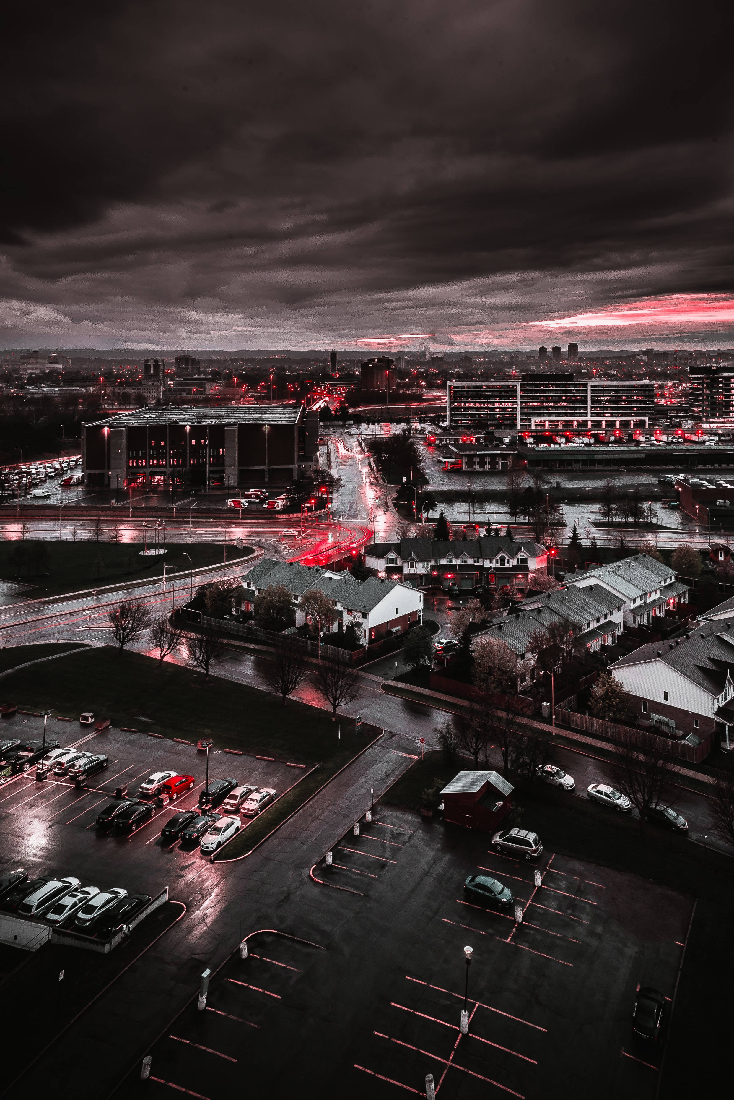 City Night 桌布 壁紙 — 黃昏時分雨中的城市擴展區鳥瞰圖，紅色霓虹燈在潮濕的街道和屋頂上反射，天空充滿氛圍感。
