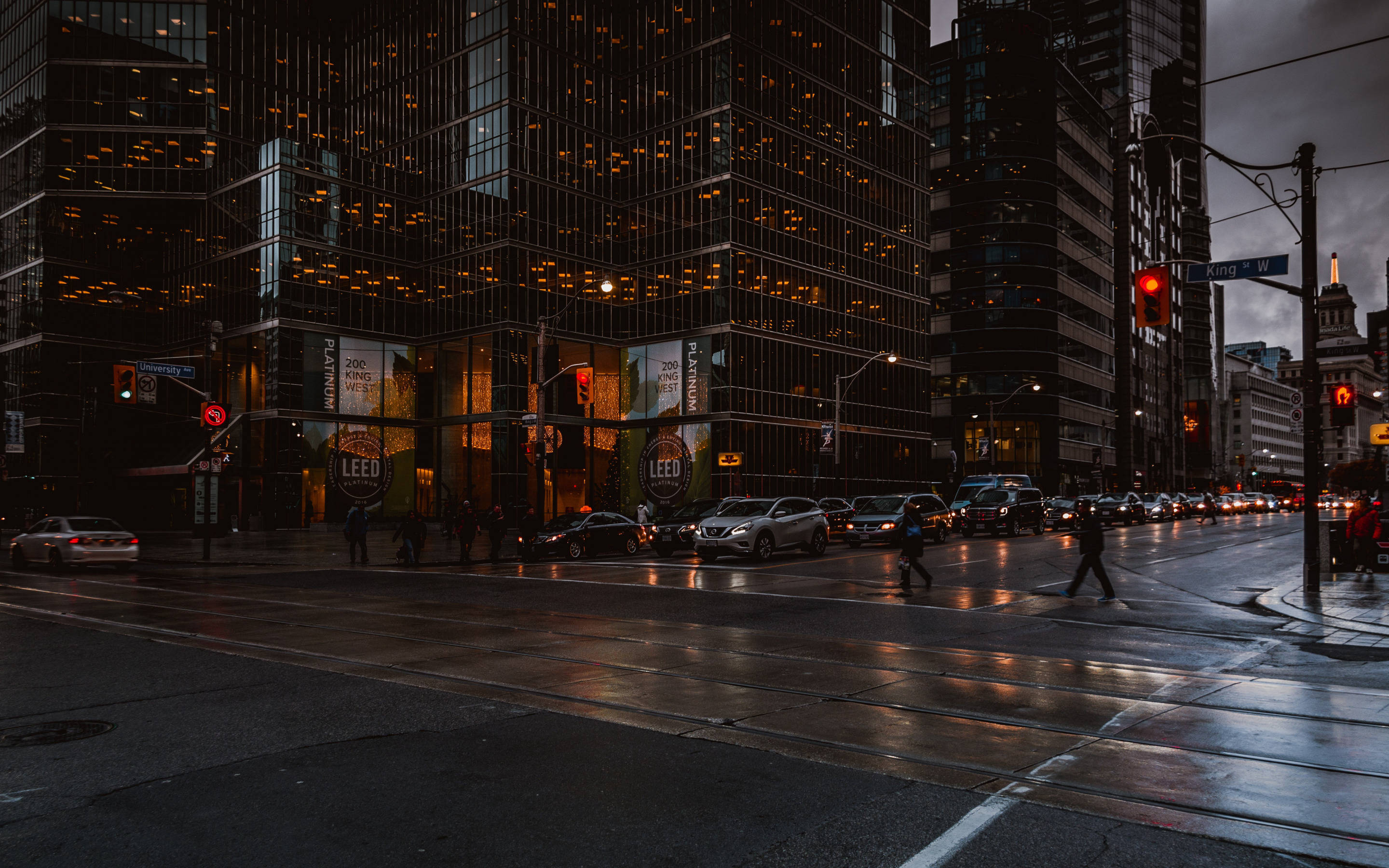 Toronto 桌布 壁紙 — 黃昏時分雨濕的城市街道，閃爍的窗戶和行人正在紅燈下過馬路。