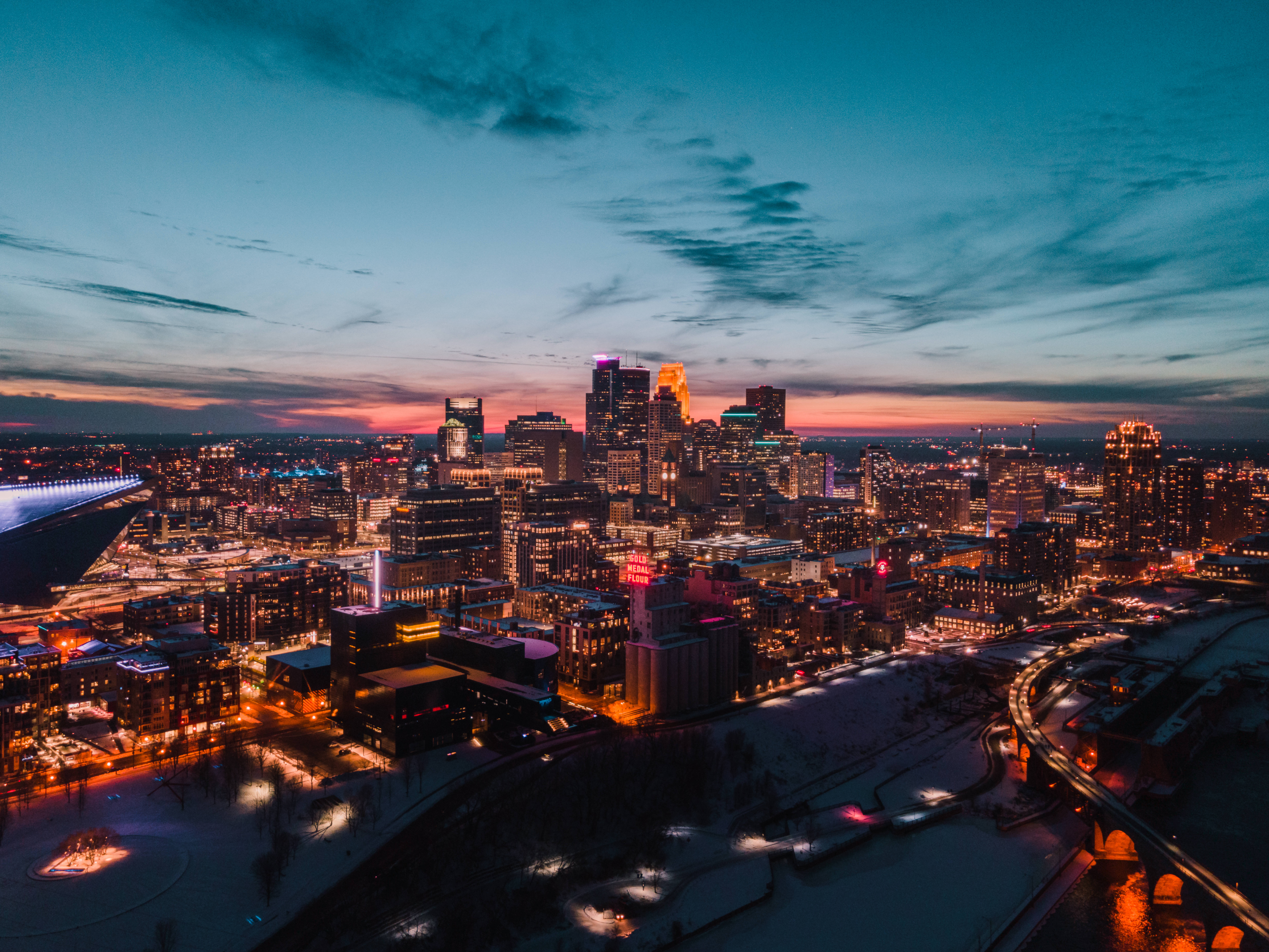 Minneapolis 桌布 壁紙 — 黃昏時分雪景城市景觀的鳥瞰圖，閃爍的摩天大樓和河流在暮色天空下反射溫暖燈光。