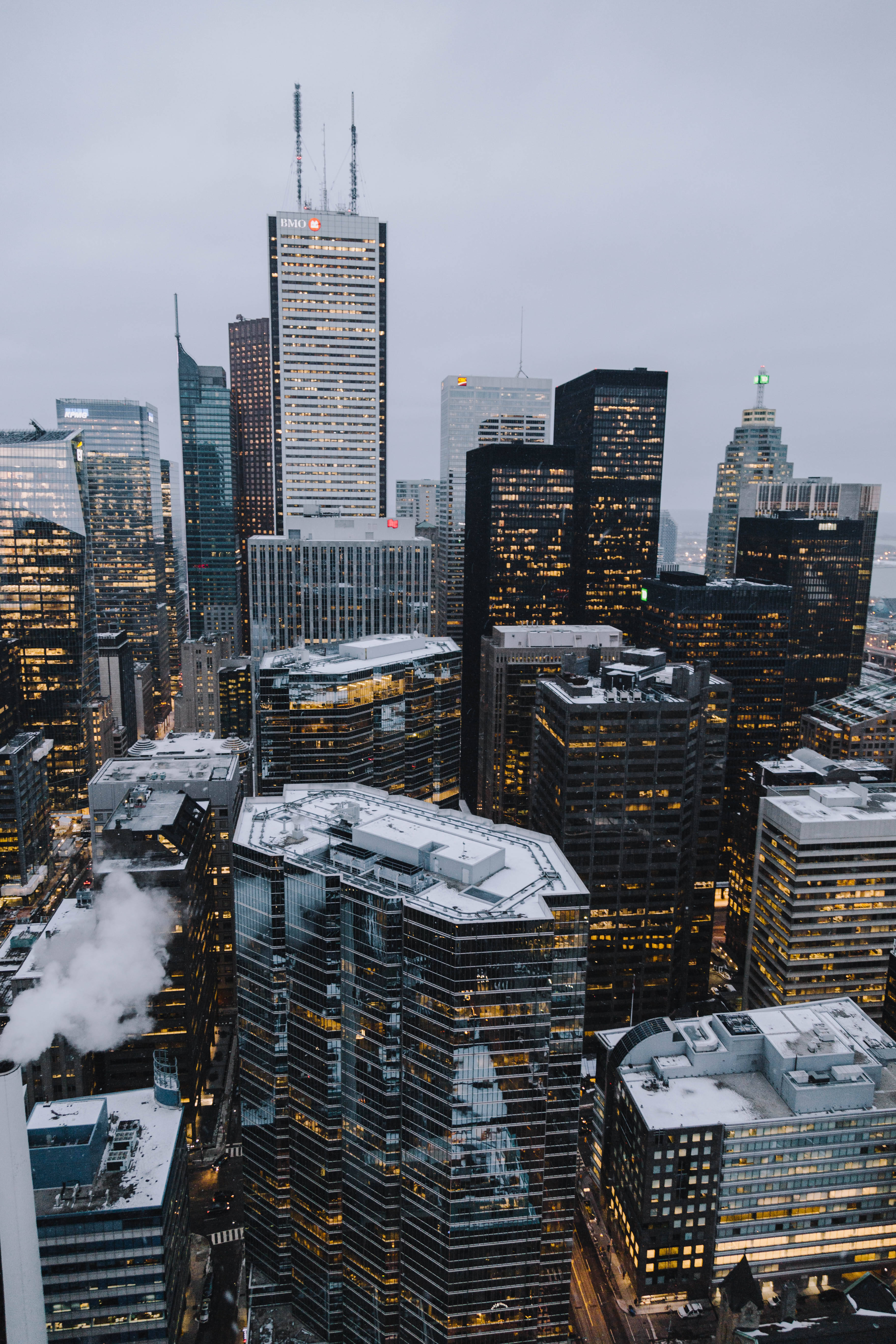 Skyscraper 桌布 壁紙 — 黃昏時分雪覆蓋的城市景觀高角度視圖，燈火通明的摩天大樓和屋頂升起的蒸汽。
