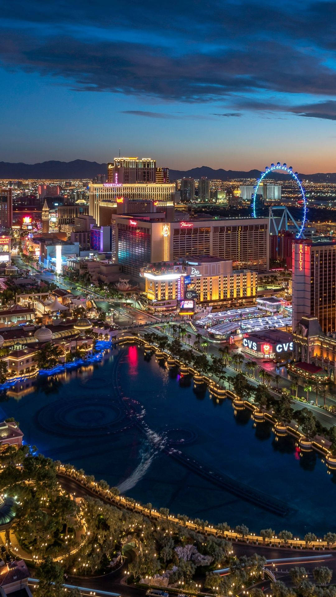 Vegas iPhone 桌布 壁紙 — 黃昏時拉斯維加斯的鳥瞰圖，發光的酒店和高滾輪摩天輪倒映在黑暗的水道中。