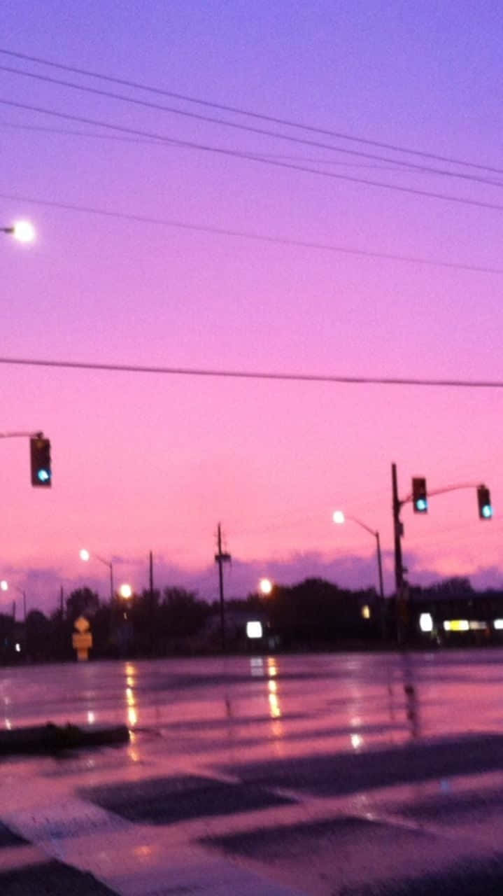 Chill Aesthetic 桌布 壁紙 — 黃昏時濕漉漉的城市街道，在充滿活力的粉紅色和紫色天空下，閃爍的交通燈倒映在雨水濕滑的路面上。