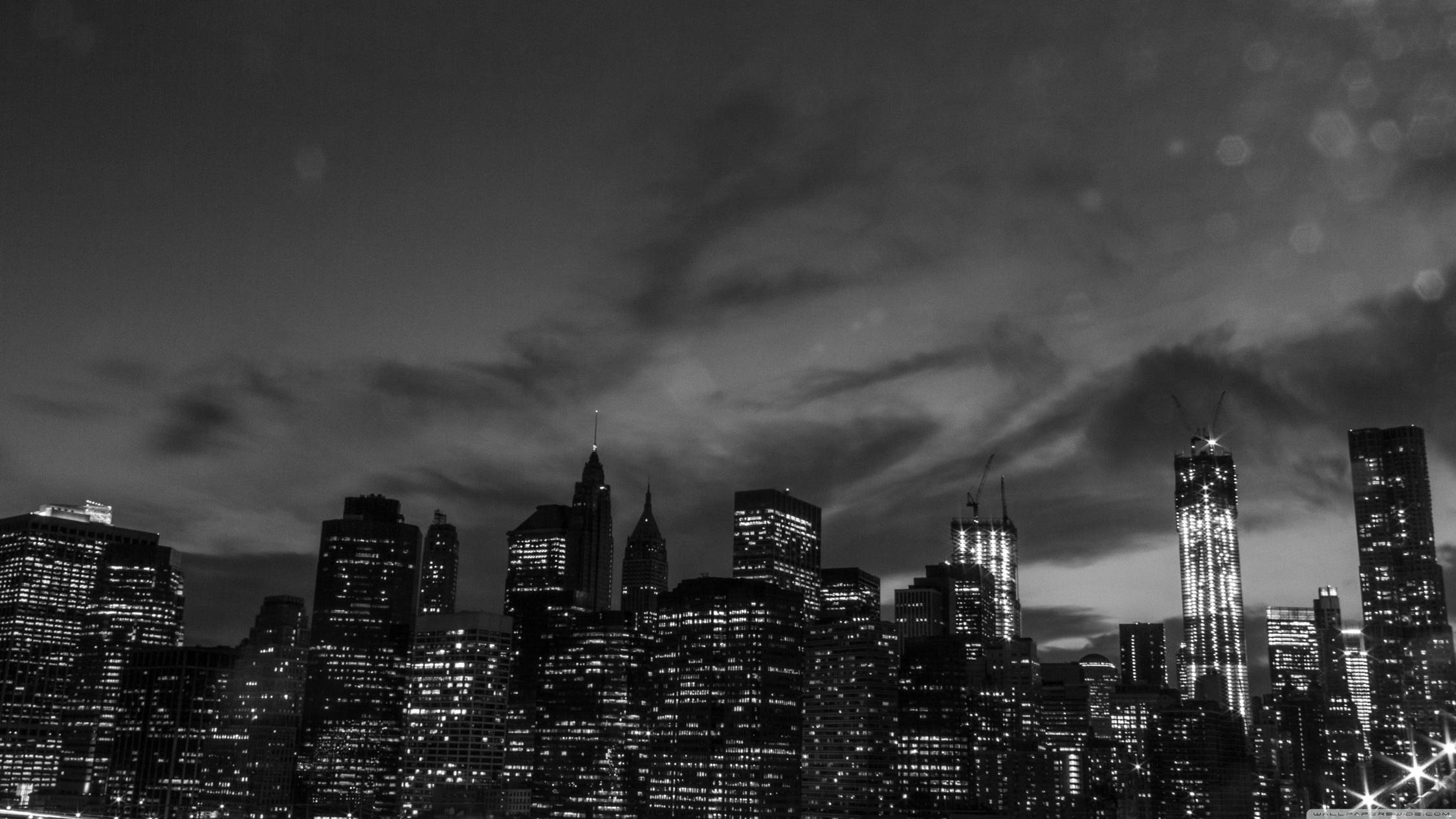 New York 桌布 壁紙 — 黃昏時的單色城市天際線，燈火通明的摩天大樓刺穿多雲的天空，帶有散景光效。