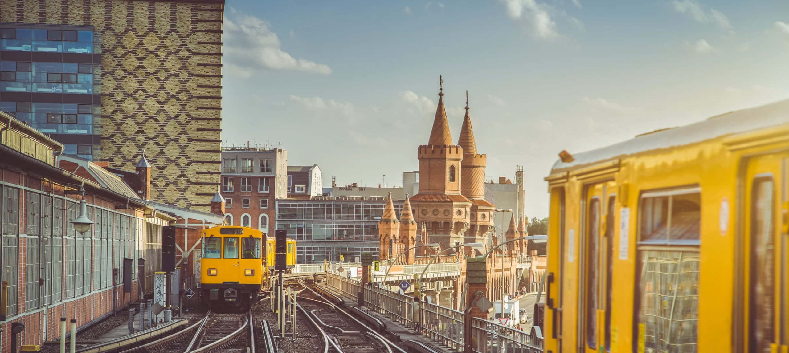 German 桌布 壁紙 — 黃色電車在明亮的天空下行駛，天空被歷史塔樓和現代建築環繞。